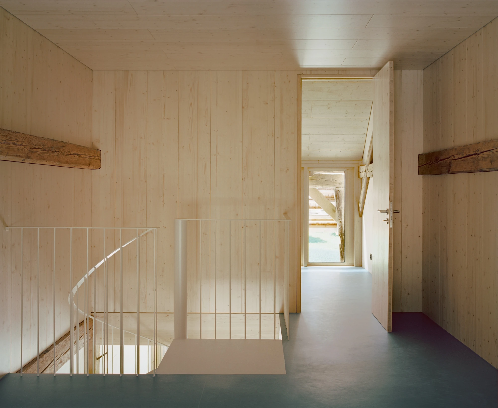 Conversion of a Farmhouse into Six Apartments by Noue Studio, photographed by Willem Pab — A timber-lined landing, a slender balustrade around the stair opening, a door open onto a corridor with a window at its end.