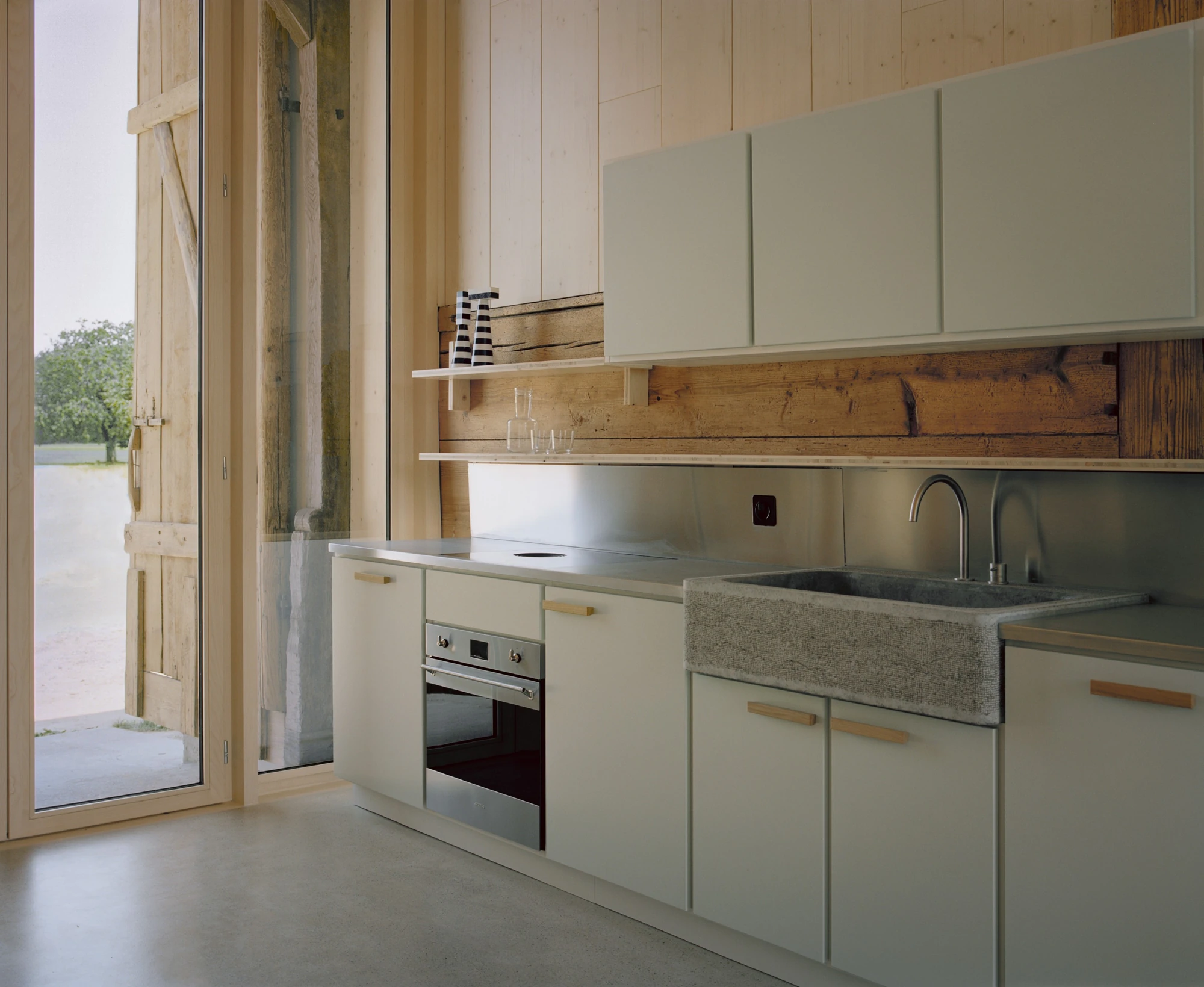 Conversion of a Farmhouse into Six Apartments by Noue Studio, photographed by Willem Pab — The compact kitchen against a timber wall, beside a floor-to-ceiling glazed door.