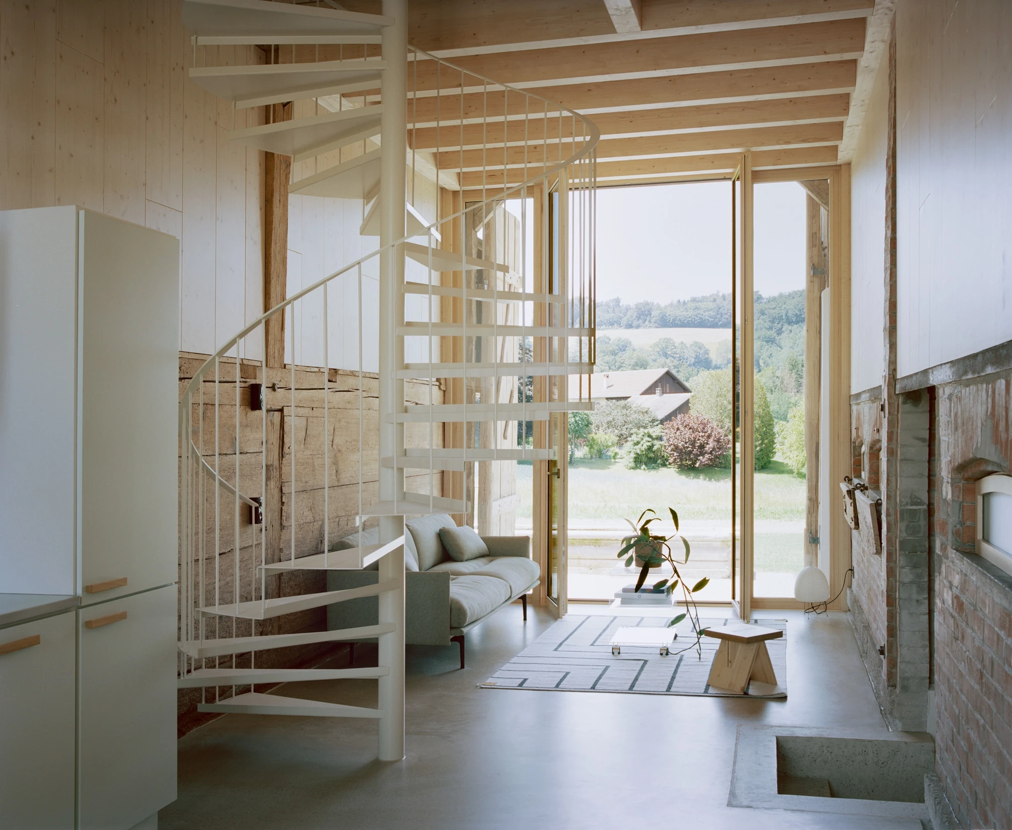 Conversion of a Farmhouse into Six Apartments by Noue Studio, photographed by Willem Pab — The pale spiral stair beside full-height glazing that opens to the surrounding land.