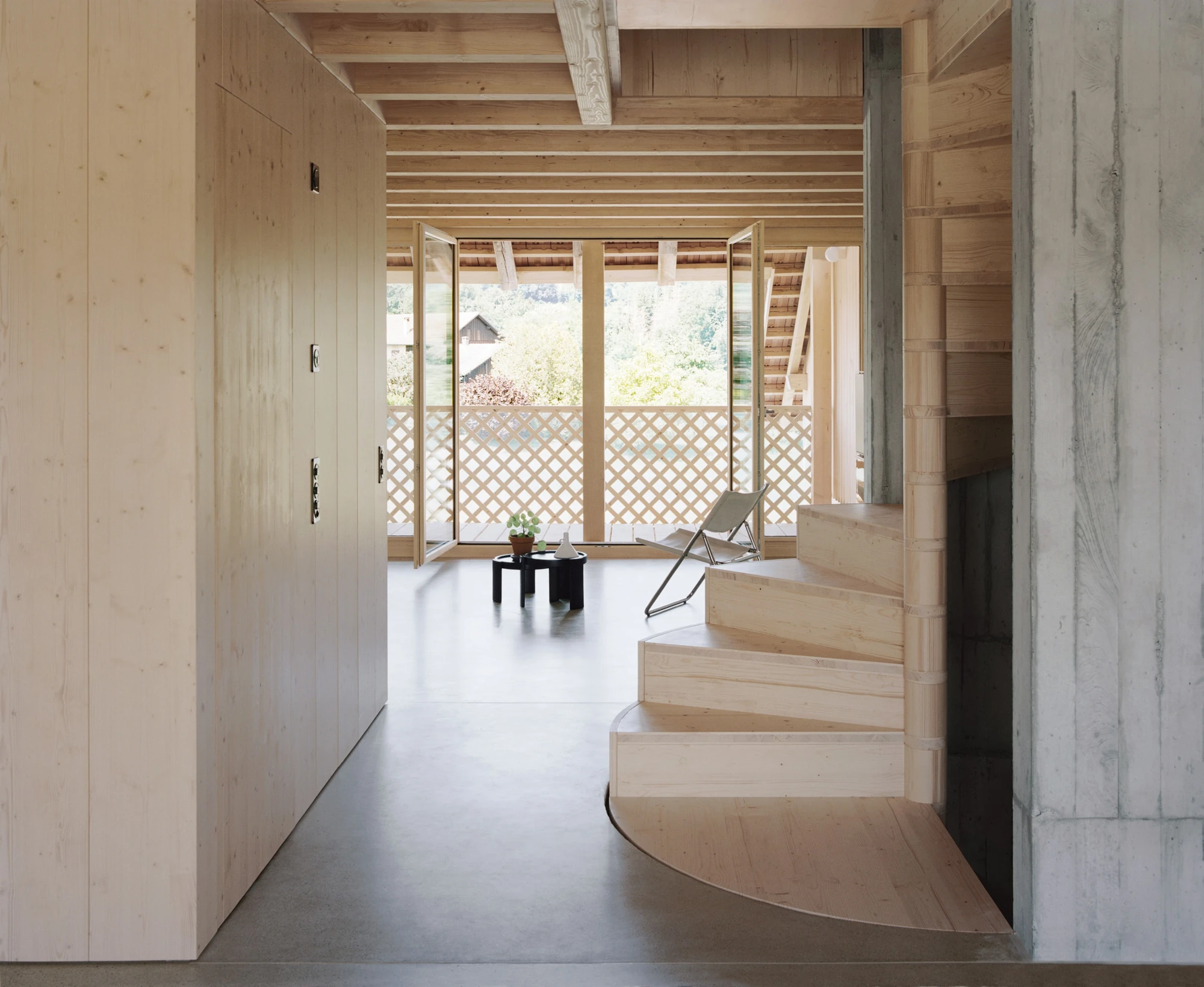 Conversion of a Farmhouse into Six Apartments by Noue Studio, photographed by Willem Pab — A room between tall built-in timber cupboards, a winding stair at right, looking out to a latticed glazed bay.