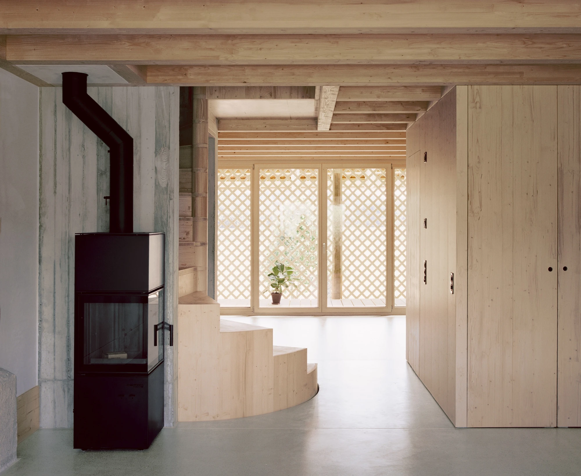 Conversion of a Farmhouse into Six Apartments by Noue Studio, photographed by Willem Pab — A living room with a freestanding stove and curved timber steps beside a latticed window.