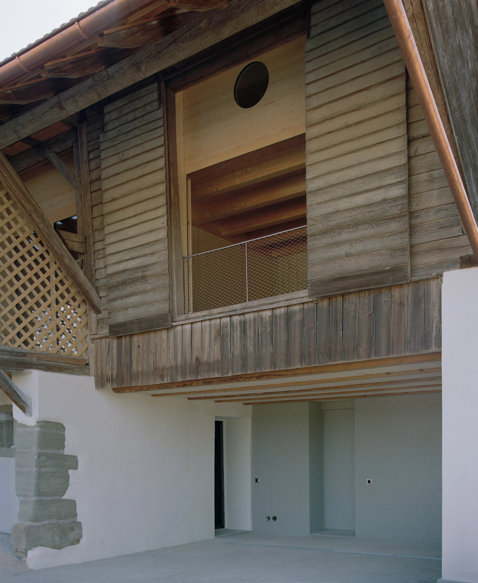 Conversion of a Farmhouse into Six Apartments by Noue Studio, photographed by Willem Pab — A weathered timber gable with a circular opening above a sheltered ground-floor recess.