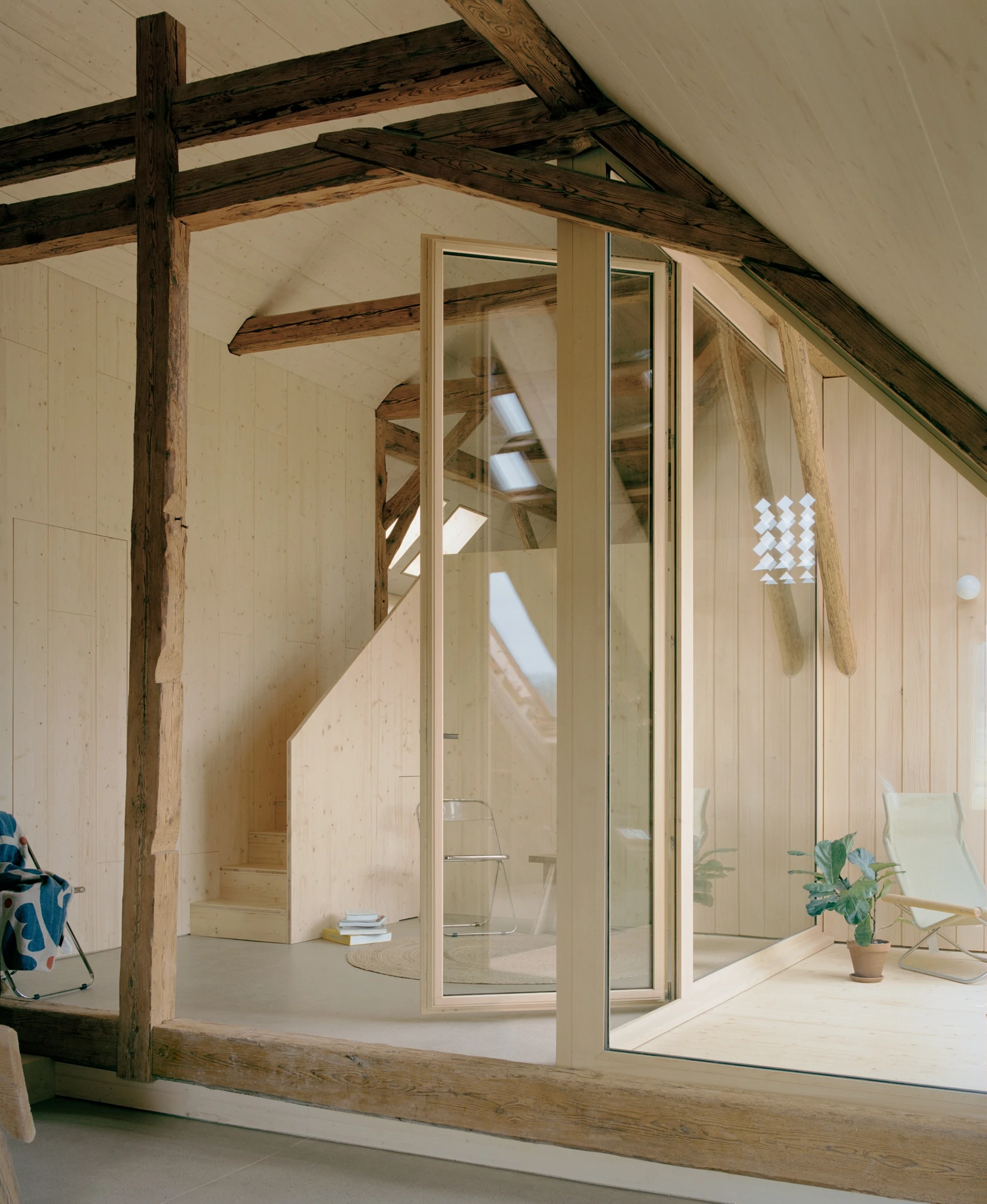 Conversion of a Farmhouse into Six Apartments by Noue Studio, photographed by Willem Pab — An attic under old timber trusses, its glazed partition folded open to an inner room.