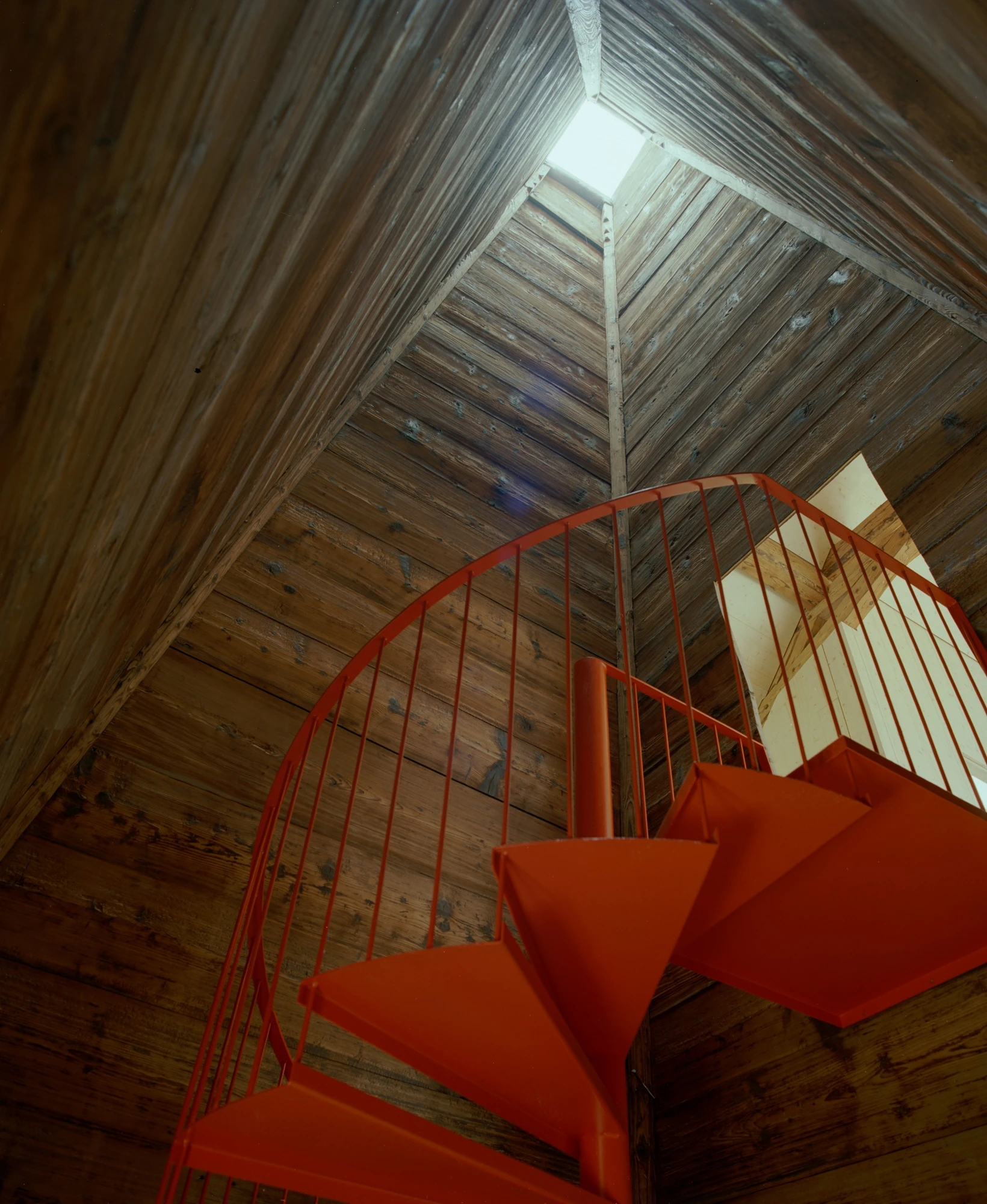 Conversion of a Farmhouse into Six Apartments by Noue Studio, photographed by Willem Pab — A spiral stair rising through a tall timber-boarded shaft toward a small rooflight.
