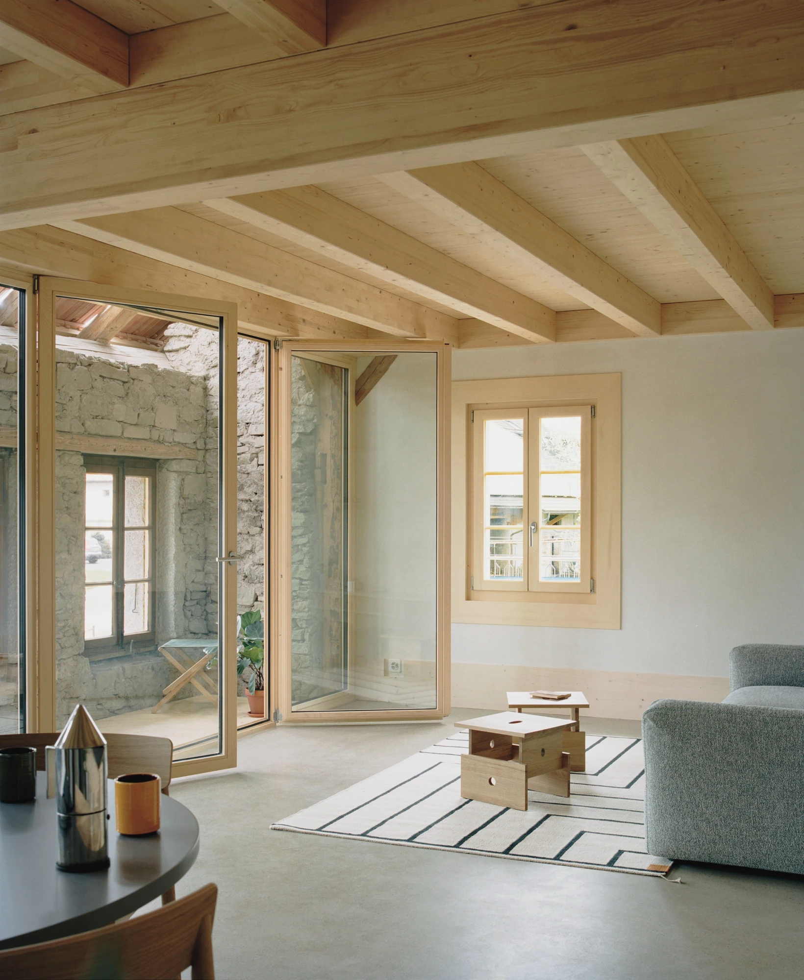 Conversion of a Farmhouse into Six Apartments by Noue Studio, photographed by Willem Pab — A living room opening through glazed doors to a preserved rough stone wall outside.