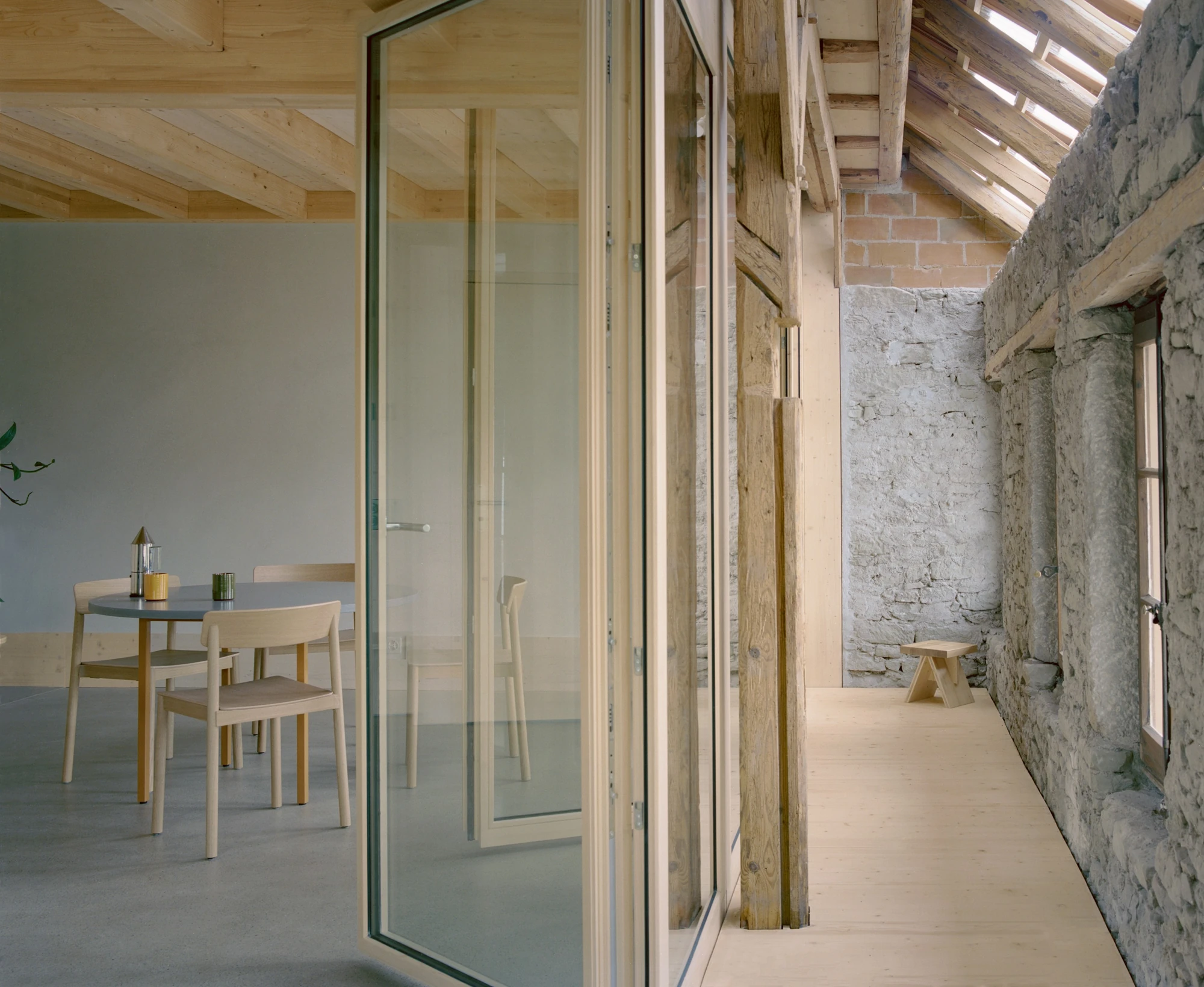 Conversion of a Farmhouse into Six Apartments by Noue Studio, photographed by Willem Pab — Folding glazed doors divide a dining room from a corridor along the old stone wall.