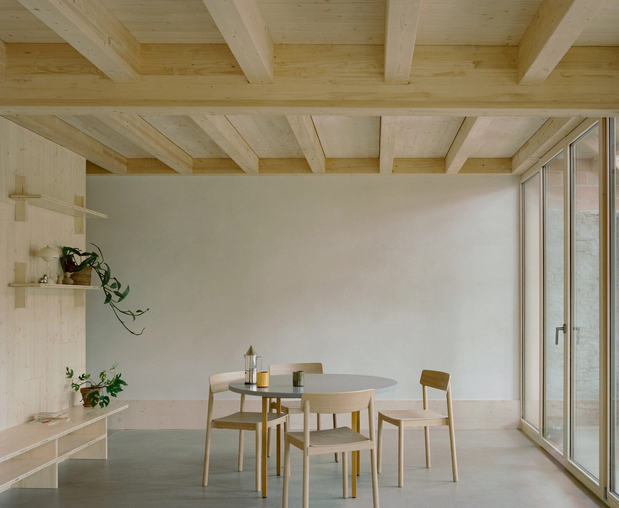 Conversion of a Farmhouse into Six Apartments by Noue Studio, photographed by Willem Pab — A dining corner beneath a timber ceiling, built-in shelves on the left wall.