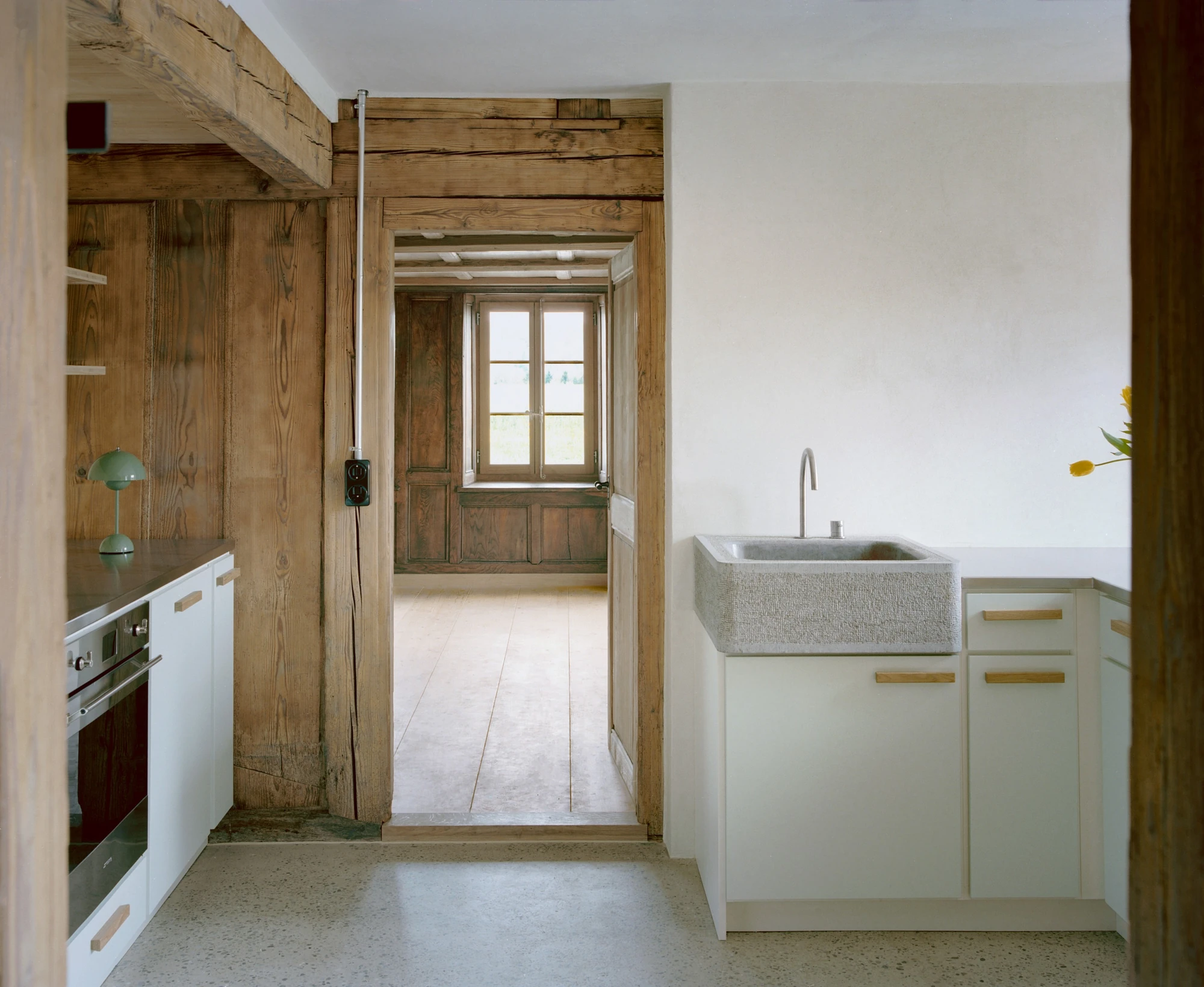 Conversion of a Farmhouse into Six Apartments by Noue Studio, photographed by Willem Pab — A kitchen with a carved stone sink and an old timber doorway leading to a panelled room.