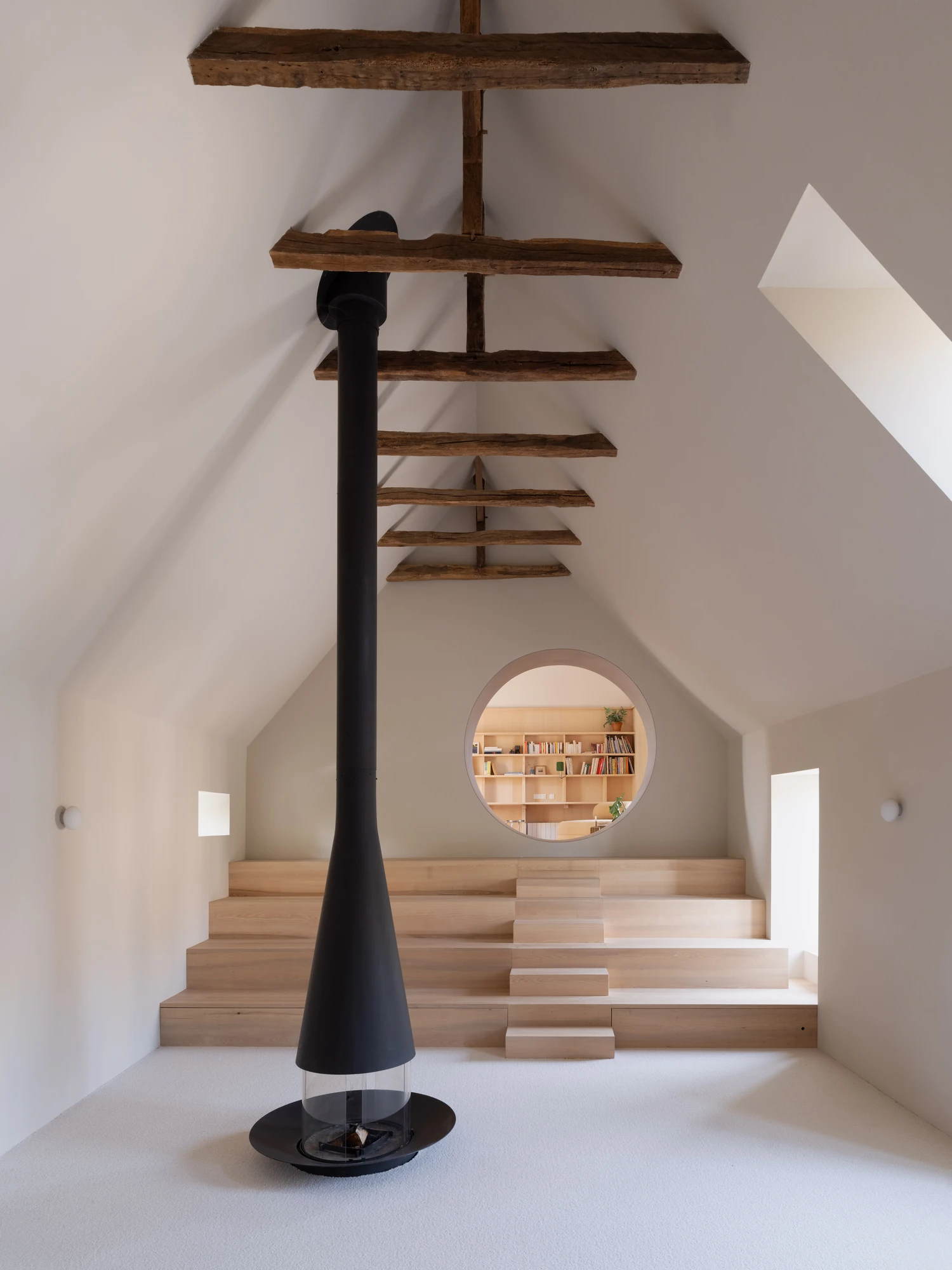 Farmhouse Renovation by Atelier AJO, photographed by Sandrine Iratçabal — The upper living room seen across its central hearth, with stepped seating rising to a circular opening cut through to the library.