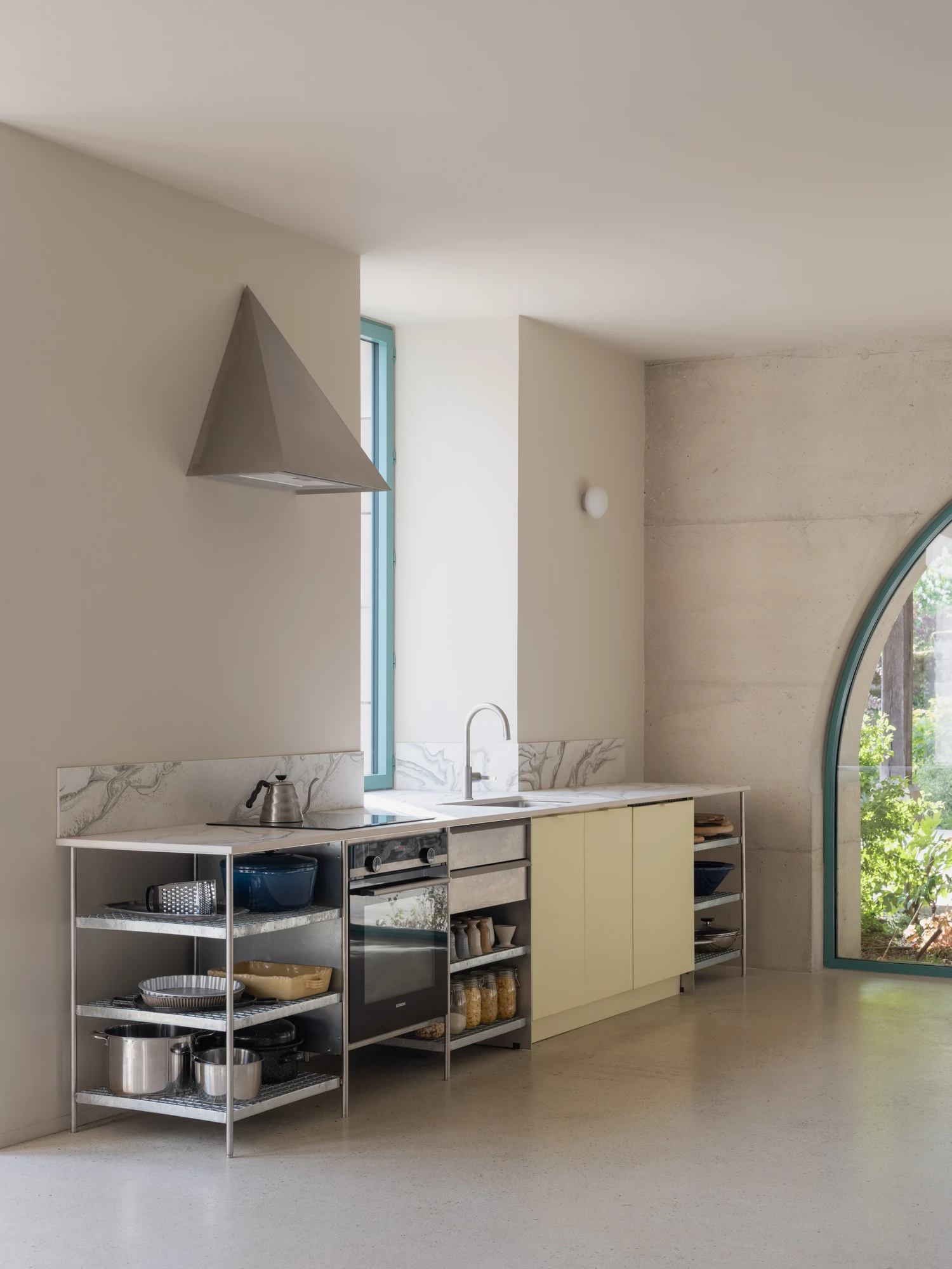 Farmhouse Renovation by Atelier AJO, photographed by Sandrine Iratçabal — The kitchen run of open shelving and cabinetry, beside an arched glazed opening to the garden.
