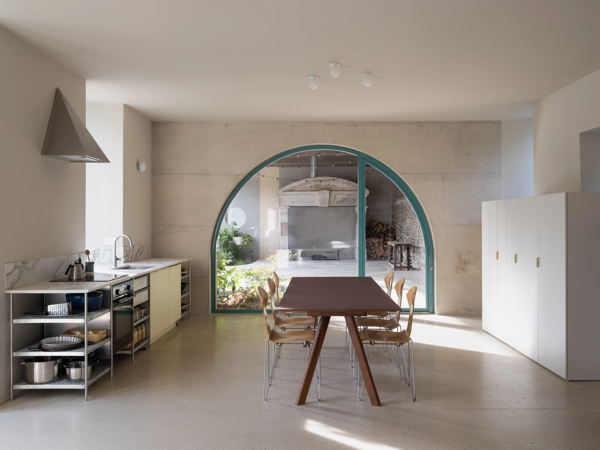Farmhouse Renovation by Atelier AJO, photographed by Sandrine Iratçabal — The dining area facing the arched opening that frames the preserved stone fireplace in the barn beyond.