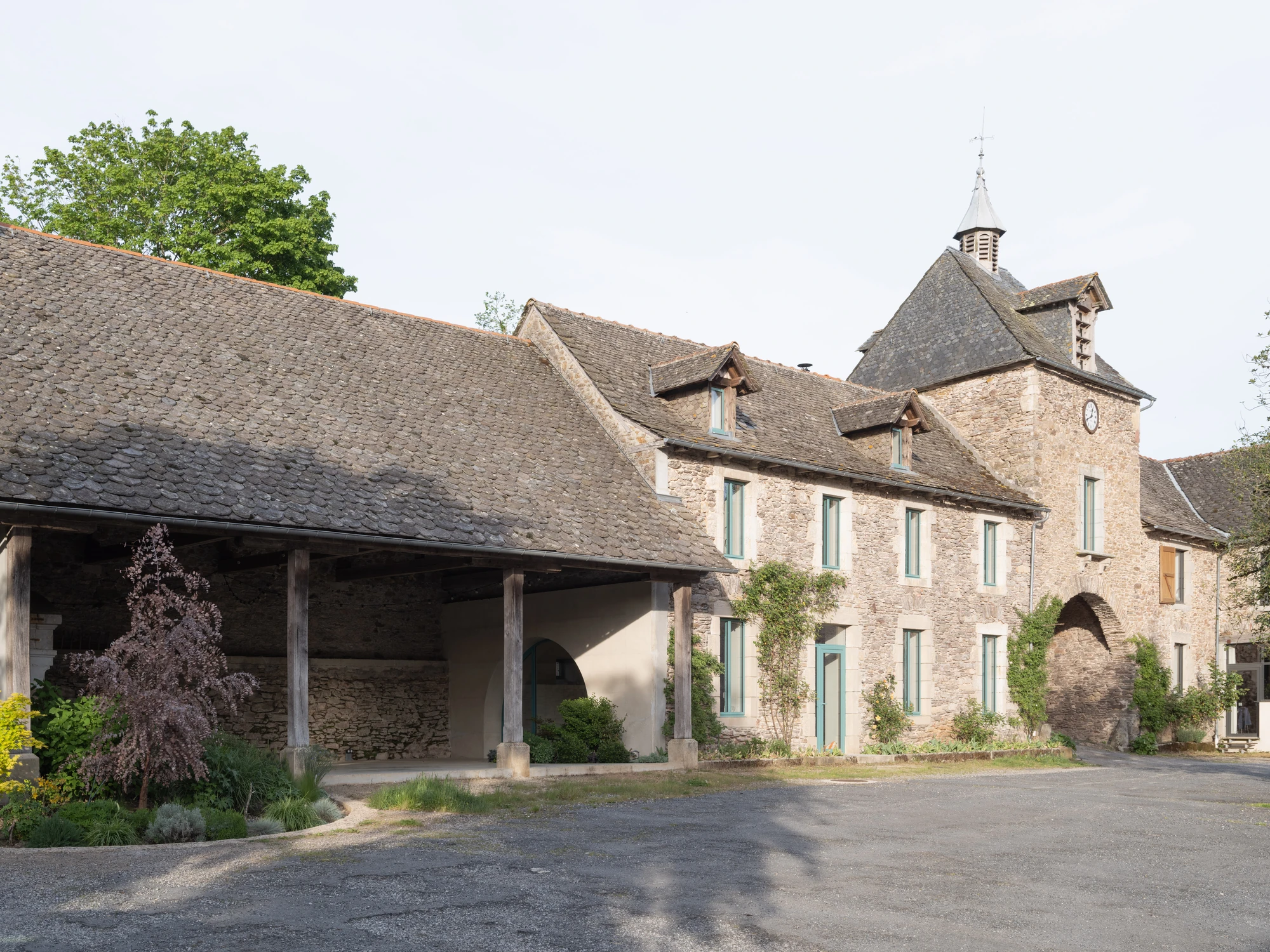 Farmhouse Renovation by Atelier AJO, photographed by Sandrine Iratçabal — The farm seen from the central courtyard, the dovecote tower at right and the open barn under its tiled roof at left.