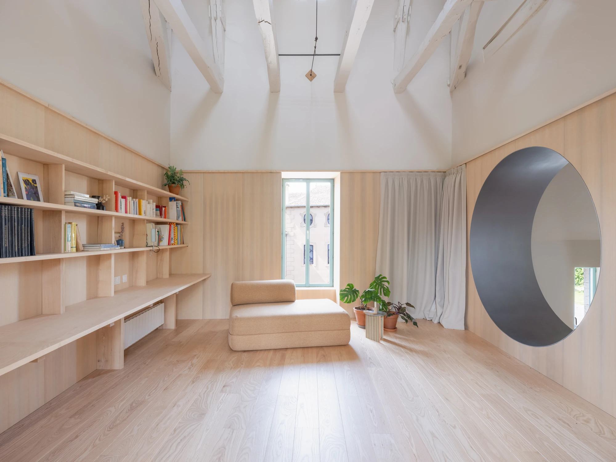 Farmhouse Renovation by Atelier AJO, photographed by Sandrine Iratçabal — The upper living room with the library wall, a tall window and the round opening set into the panelling.