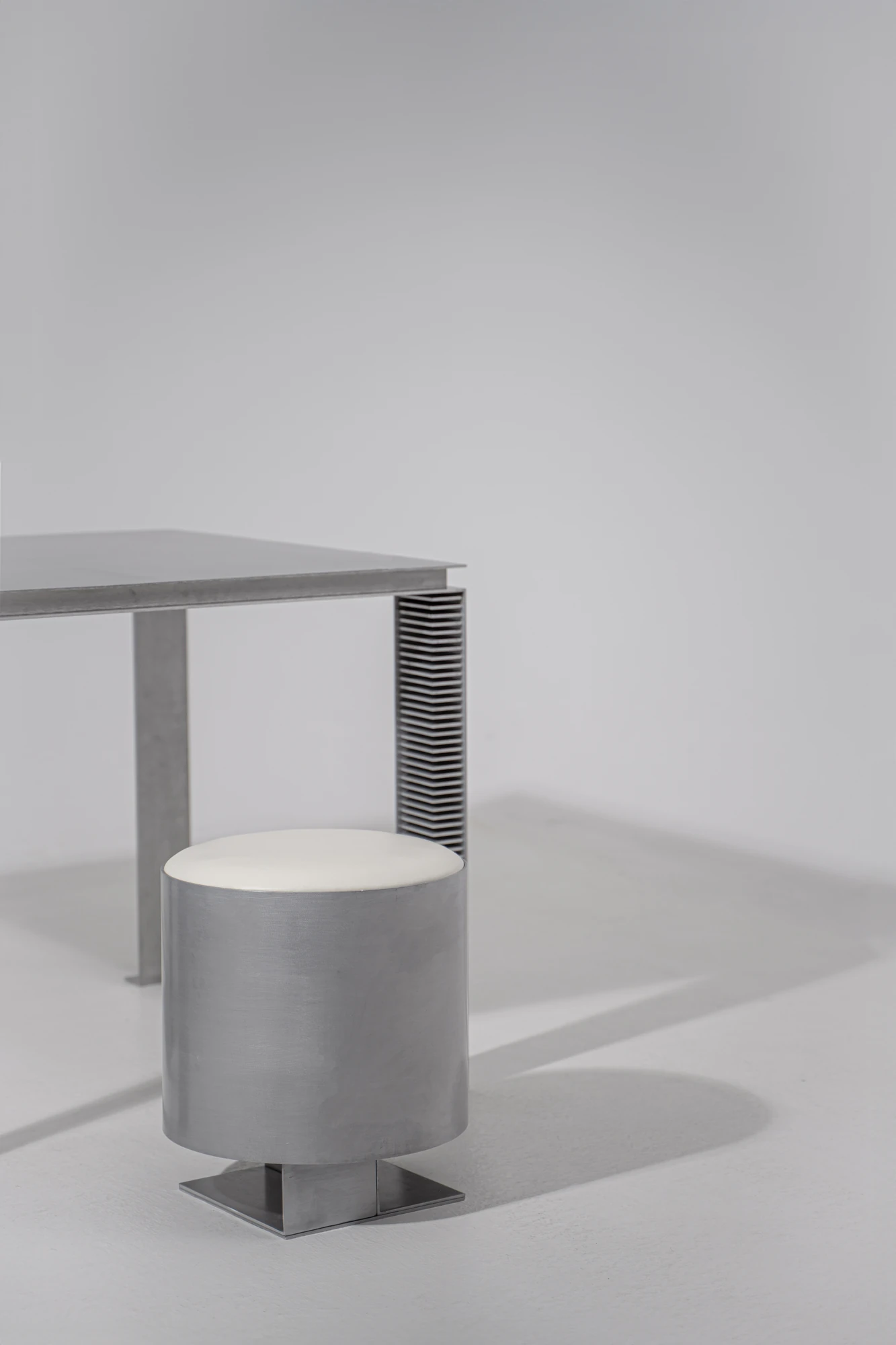 Strut Collection by YET. Design Studio, photographed by Kaan Bayoglu — The Strut Pouf beside the Strut Table, whose leg reveals a stack of repeated aluminium angle profiles.