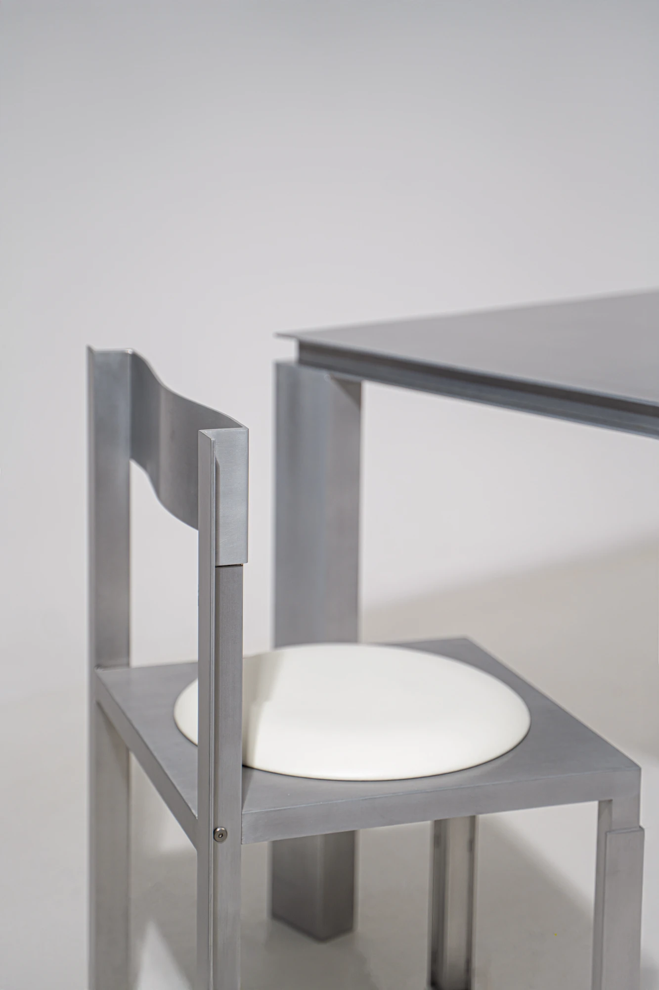 Strut Collection by YET. Design Studio, photographed by Kaan Bayoglu — A corner view of the Strut Chair pulled up to the Strut Table, the chair's circular seat inset in its frame.