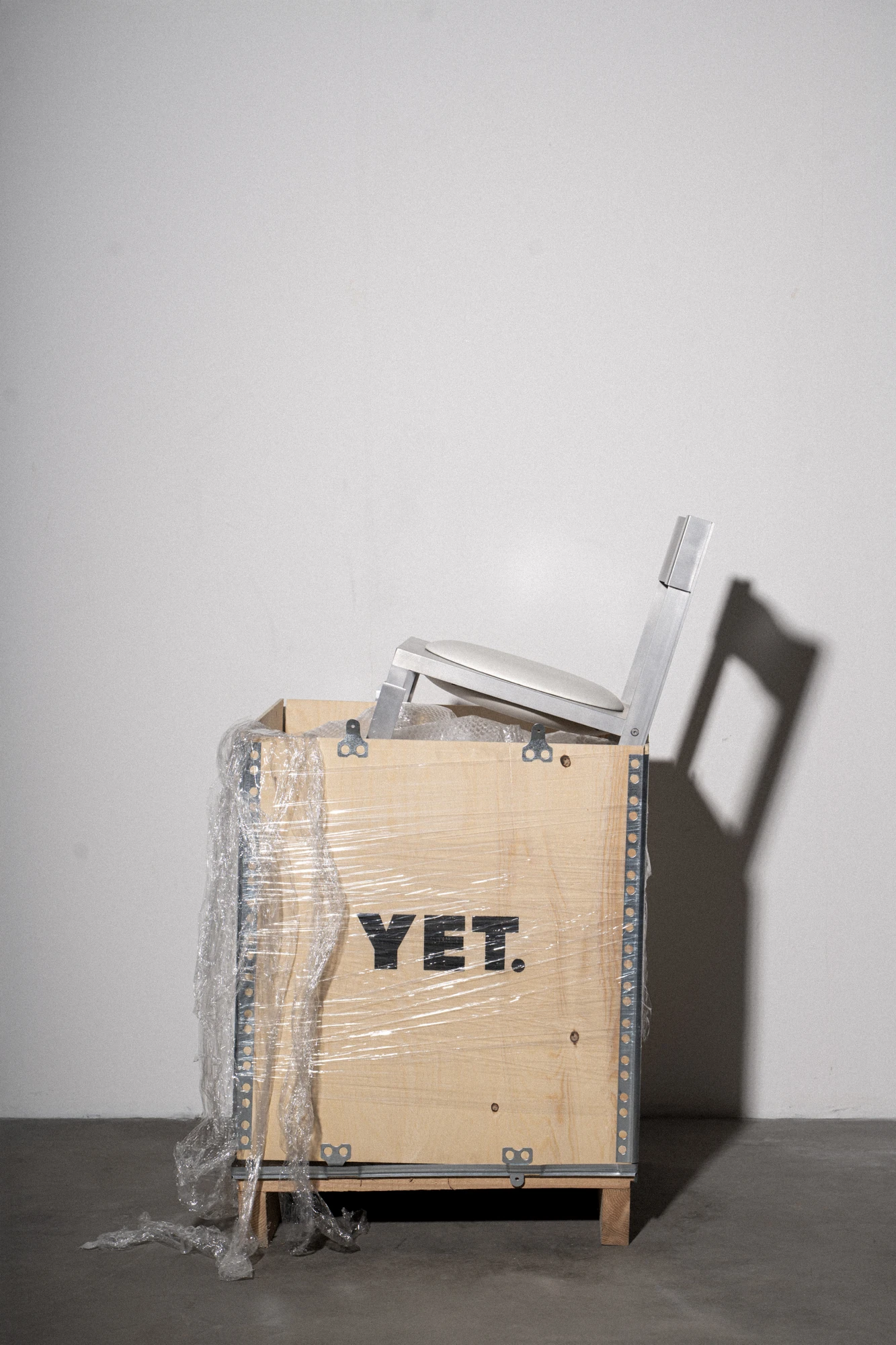 Strut Collection by YET. Design Studio, photographed by Kaan Bayoglu — The Strut Chair rising from the studio's shipping crate marked YET, its shadow thrown on the wall behind.