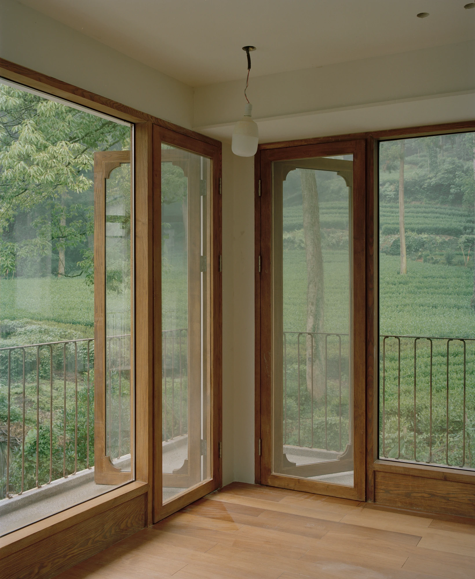 L Hermit House II by Common Wonder, photographed by Willem Pab, Eva Candela — Two timber-framed doors meeting at a corner, opening the room to the tea fields on both sides.