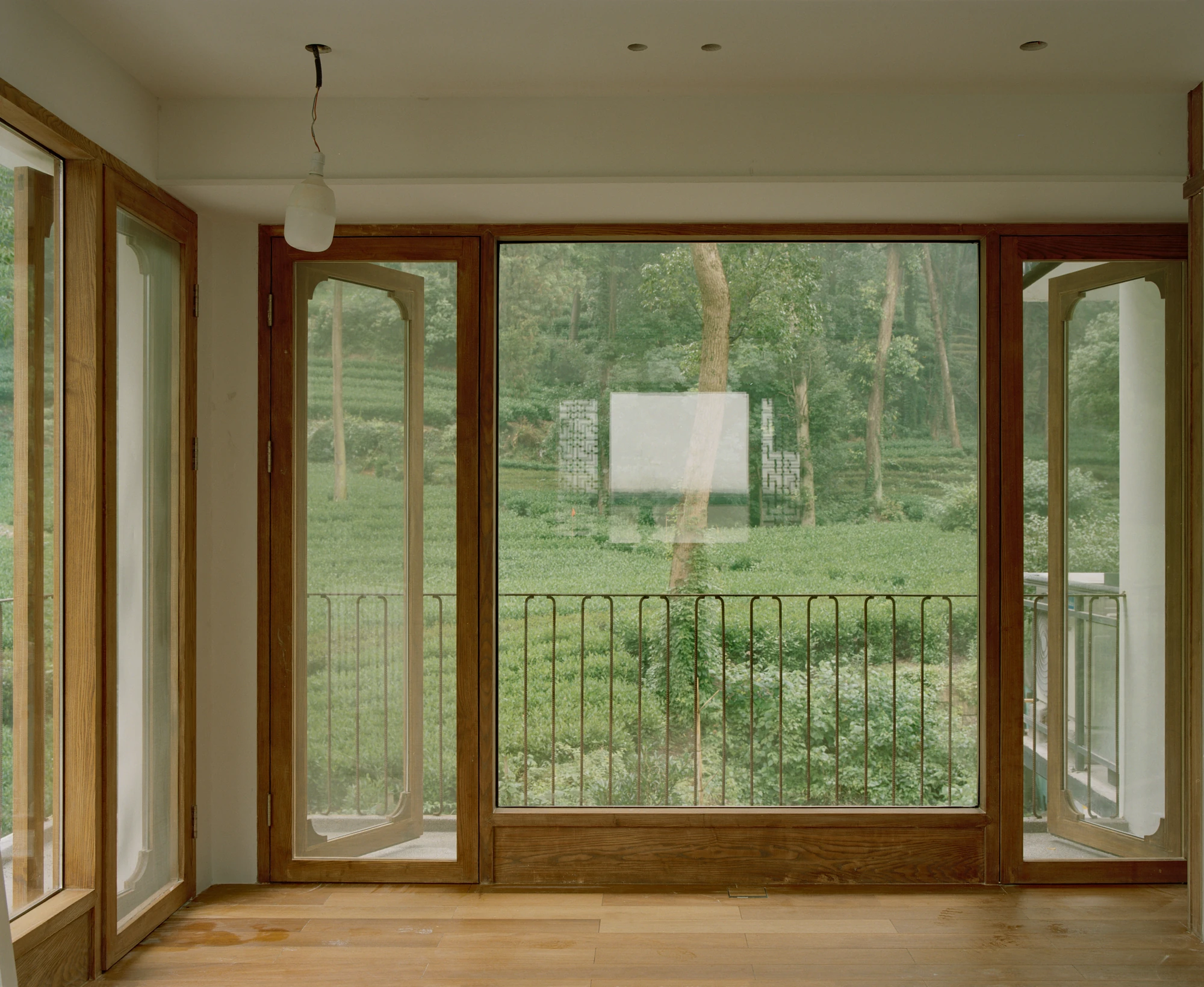 L Hermit House II by Common Wonder, photographed by Willem Pab, Eva Candela — A large glazed opening with timber-framed doors giving onto a balcony above the tea fields.