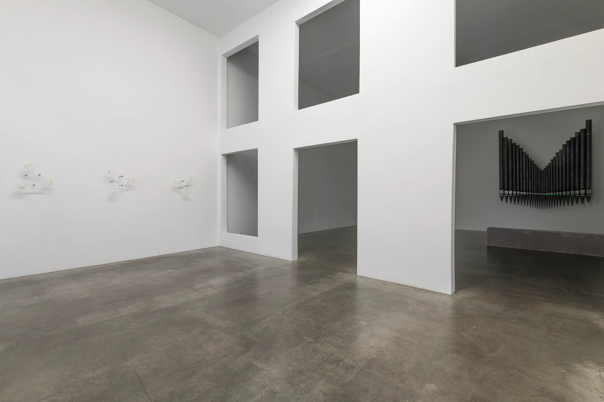 Half-Life of Grace by Jeremy Shaw, photographed by Stefan Korte — Installation view across the two rooms, the small glass works at left and the organ-pipe sculpture visible through a doorway at right.