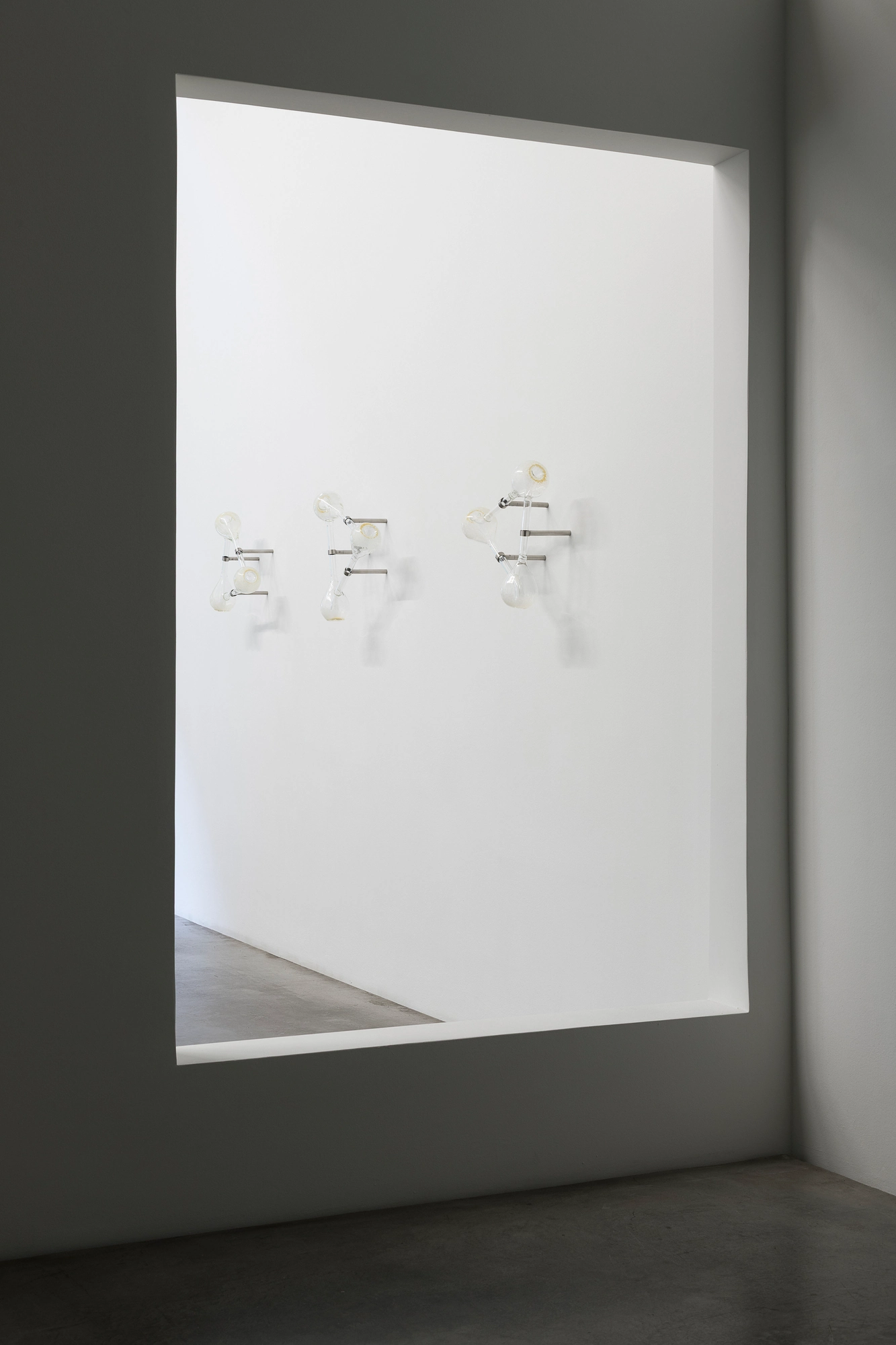 Half-Life of Grace by Jeremy Shaw, photographed by Stefan Korte — Installation view looking through a wall opening to the three glass Klein-bottle sculptures in the first room.