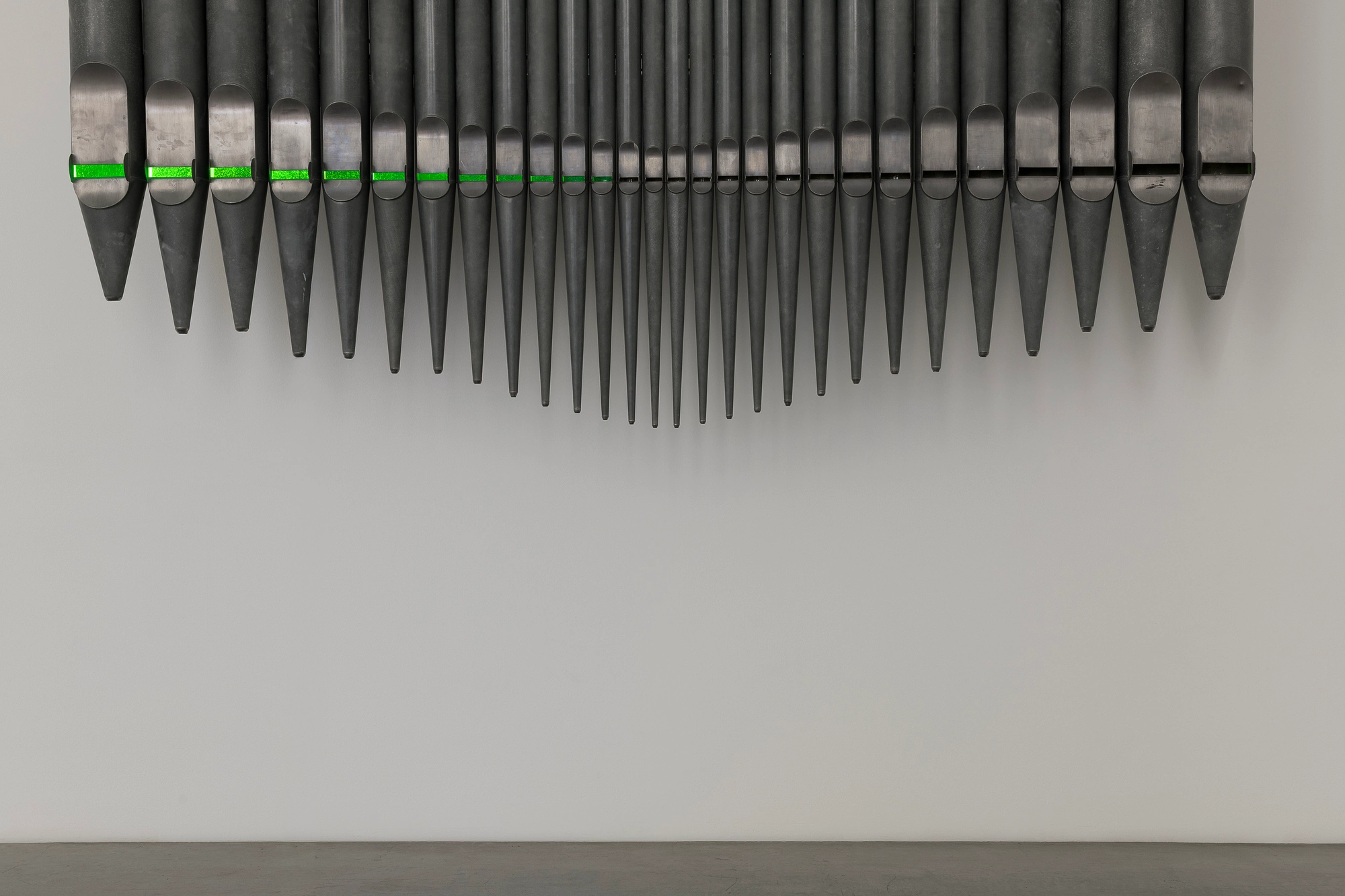 Half-Life of Grace by Jeremy Shaw, photographed by Stefan Korte — Detail of the organ pipes from below, tapered feet in a row with green light glowing at the pipe mouths above.