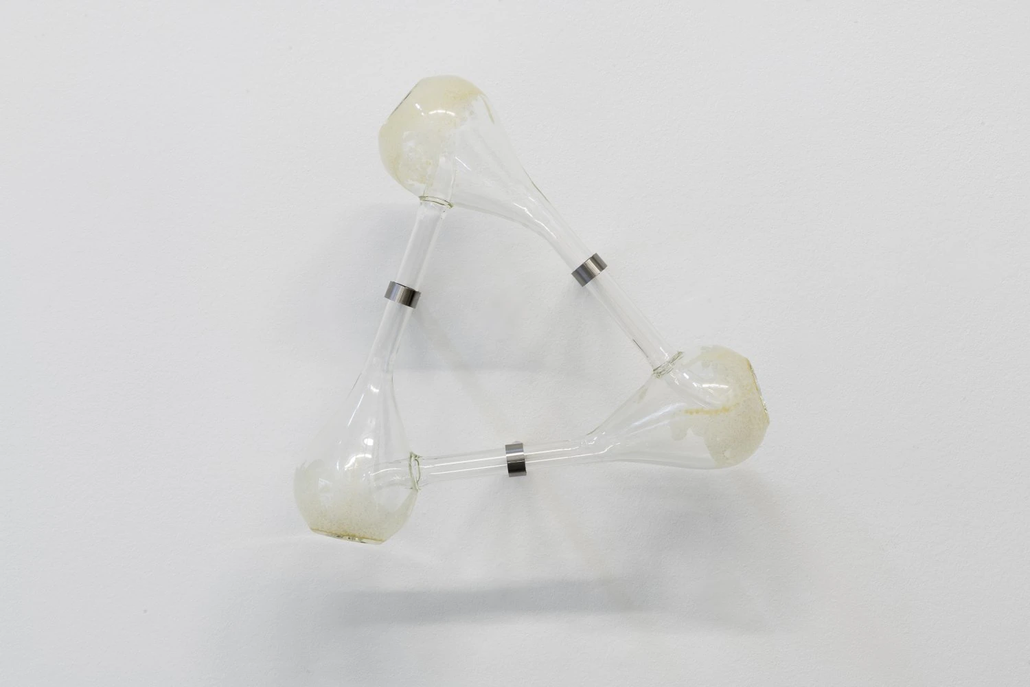 Half-Life of Grace by Jeremy Shaw, photographed by Stefan Korte — Innumerable Thresholds Remain Available to You Without End, a closed loop of three glass Klein bottles joined by tubes and stainless steel bands.