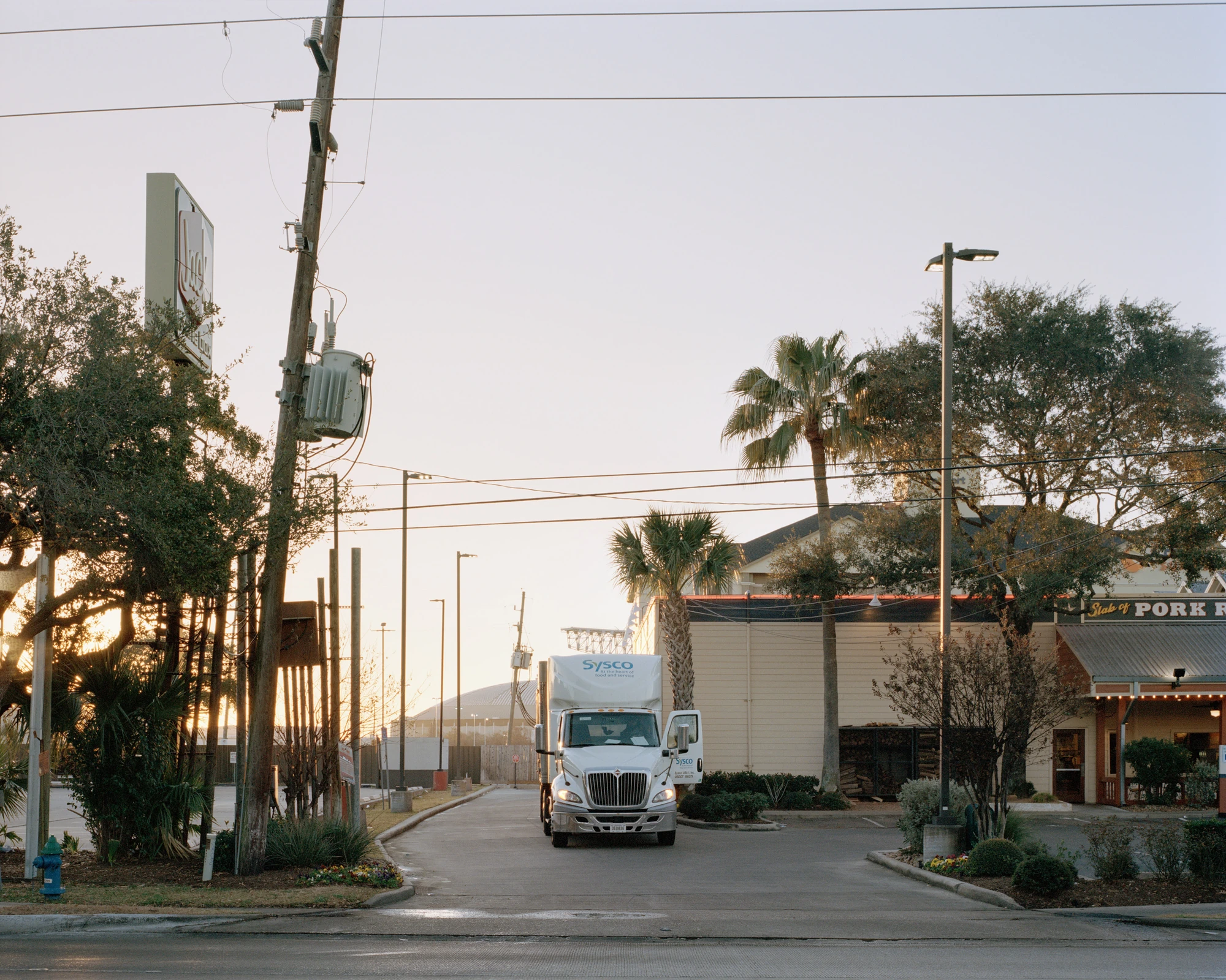 Houston, Untitled by Rory Gardiner, photographed by Rory Gardiner — 29.690439, -95.417416: a truck stands at a street corner, trees and low buildings framing the road.