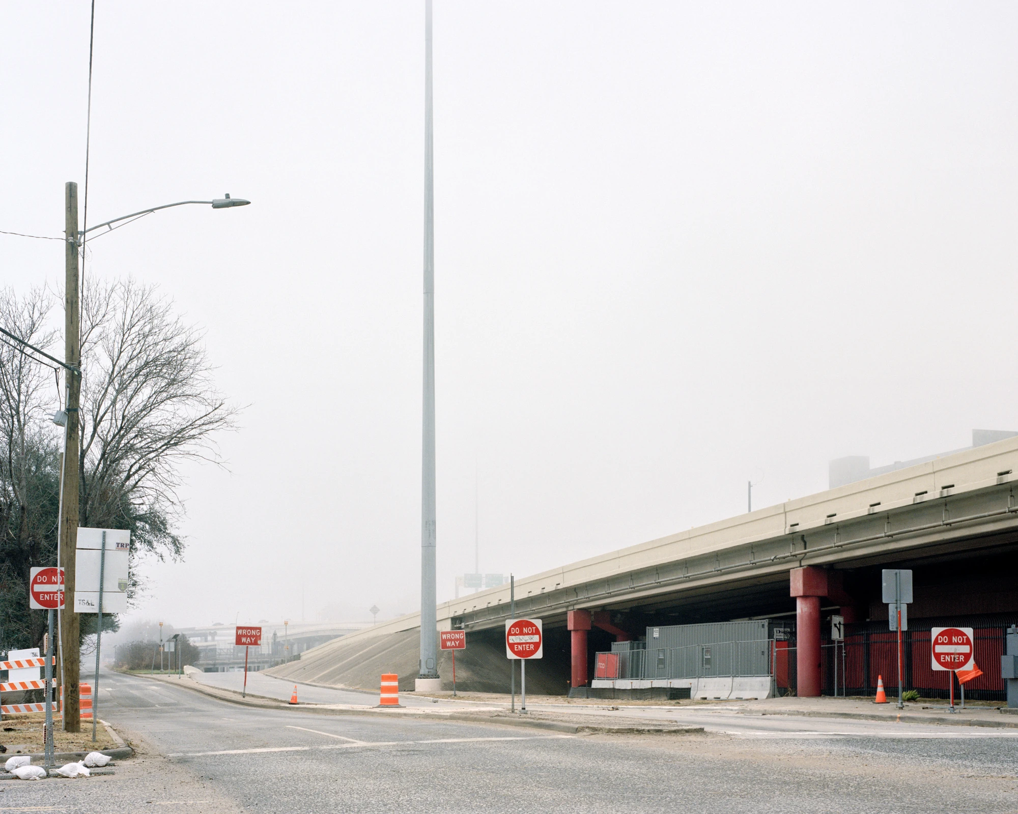 Houston, Untitled by Rory Gardiner, photographed by Rory Gardiner — 29.749394, -95.358120: a road vanishes into fog beside a motorway flyover, Do Not Enter and Wrong Way signs clustered at the junction.