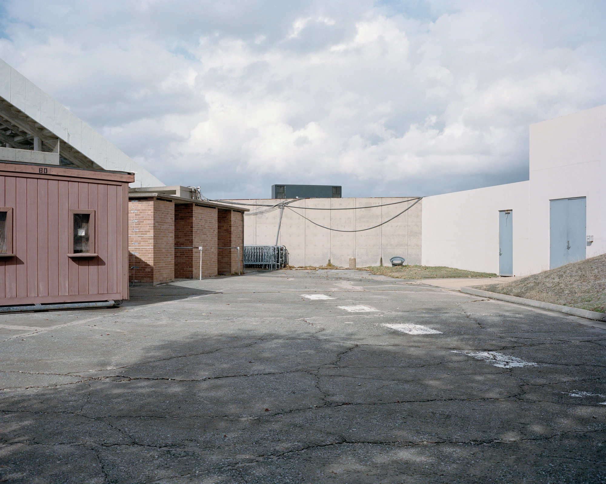Houston, Untitled by Rory Gardiner, photographed by Rory Gardiner — 29.715263, -95.409854: an empty car park between low buildings and a concrete wall.