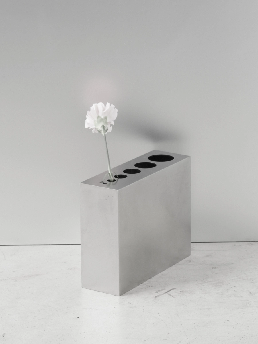 Apropos VASE-21 by Non-Objective, photographed by Elena Gavrilenko — A single white flower standing in one opening of VASE-21, the stainless steel top and its row of openings behind