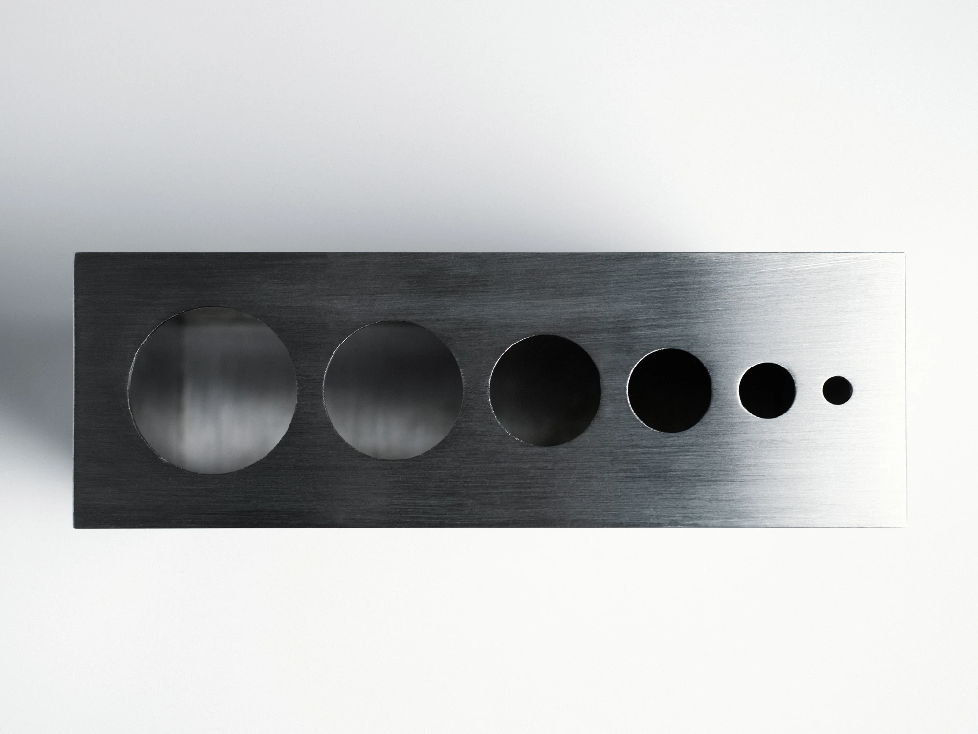 Apropos VASE-21 by Non-Objective, photographed by Elena Gavrilenko — VASE-21 seen from directly above, six round openings stepping down in size across the stainless steel top