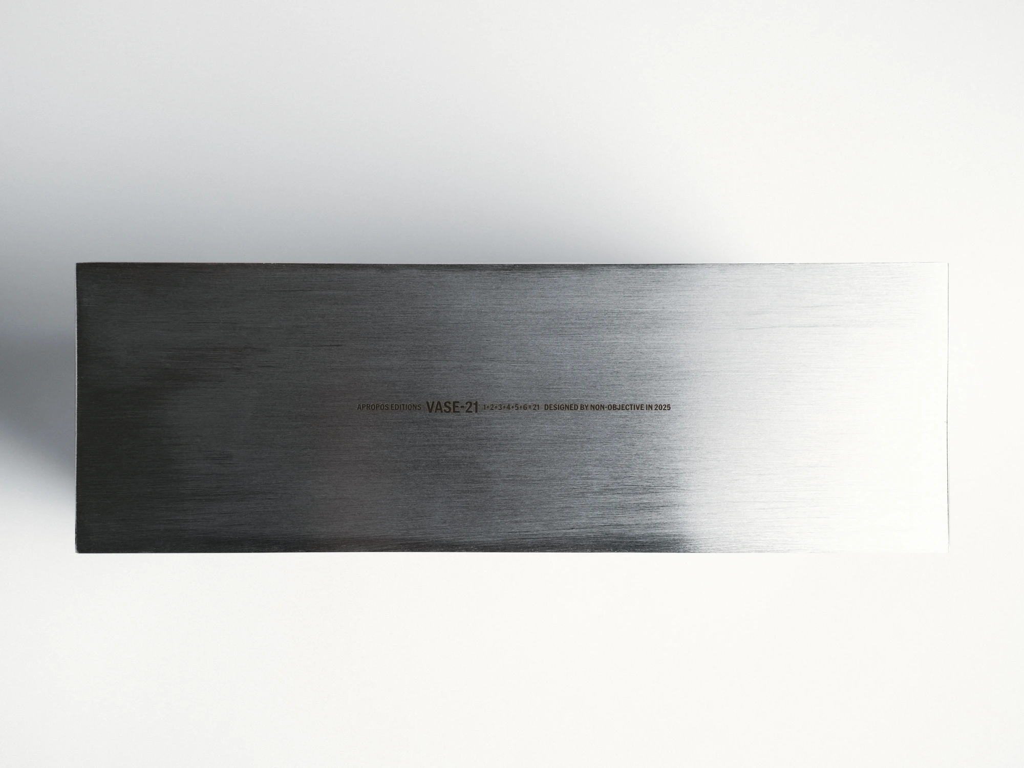 Apropos VASE-21 by Non-Objective, photographed by Elena Gavrilenko — VASE-21 laid flat, a single engraved line of text running across the brushed stainless steel face
