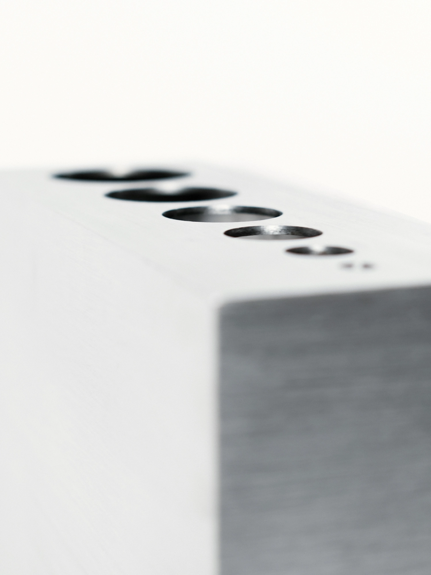 Apropos VASE-21 by Non-Objective, photographed by Elena Gavrilenko — Angled close view along the top of VASE-21, the row of openings receding from large to small in the stainless steel