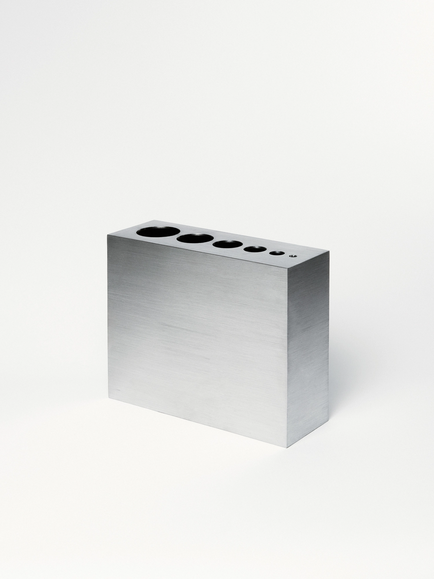 Apropos VASE-21 by Non-Objective, photographed by Elena Gavrilenko — VASE-21 empty on a white ground, a three-quarter view of the stainless steel top and its row of openings