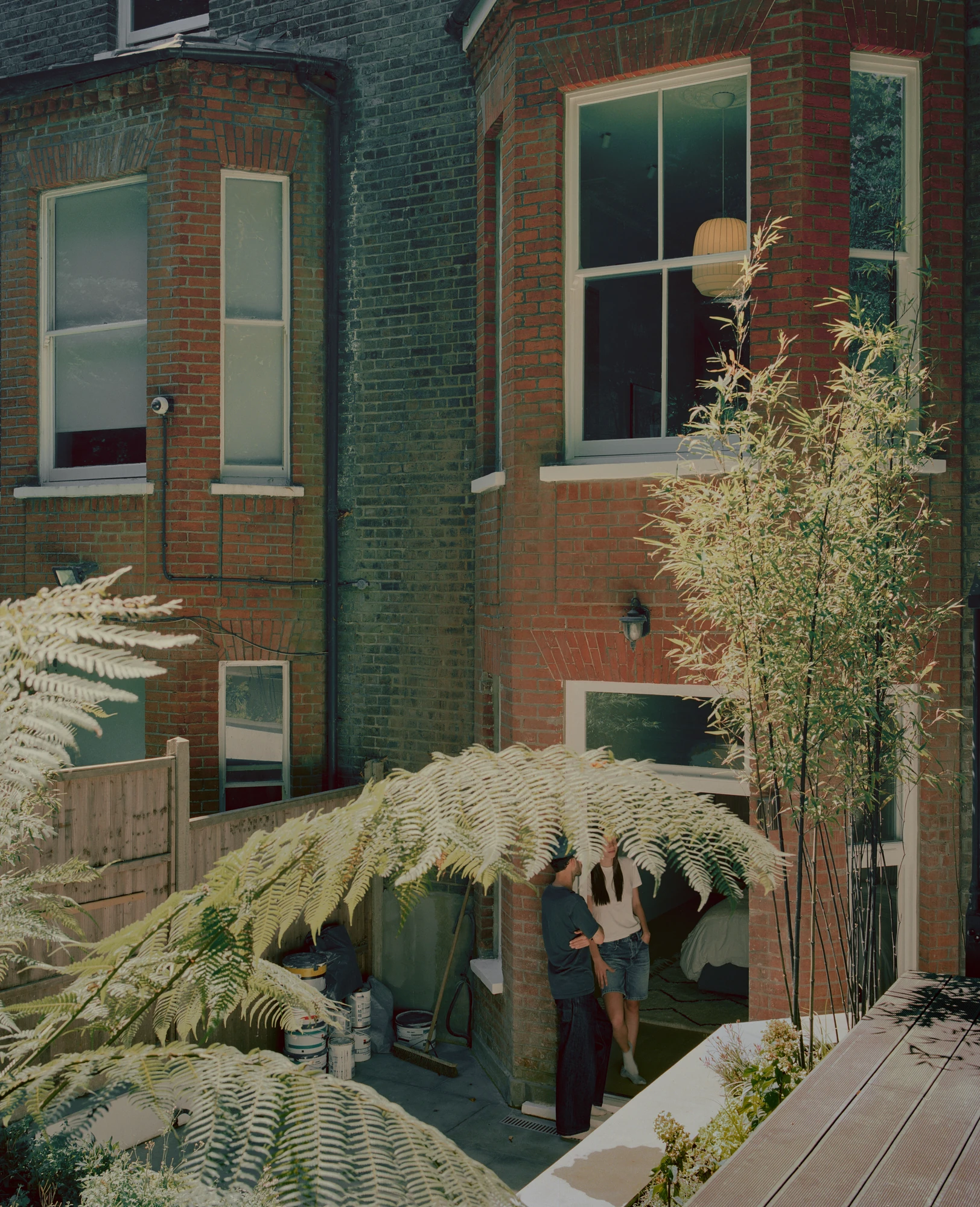 Hampstead House by Twelve Forty One, photographed by Willem Pab — The rear of the house from the garden, two figures by the door and the bay window lit above.