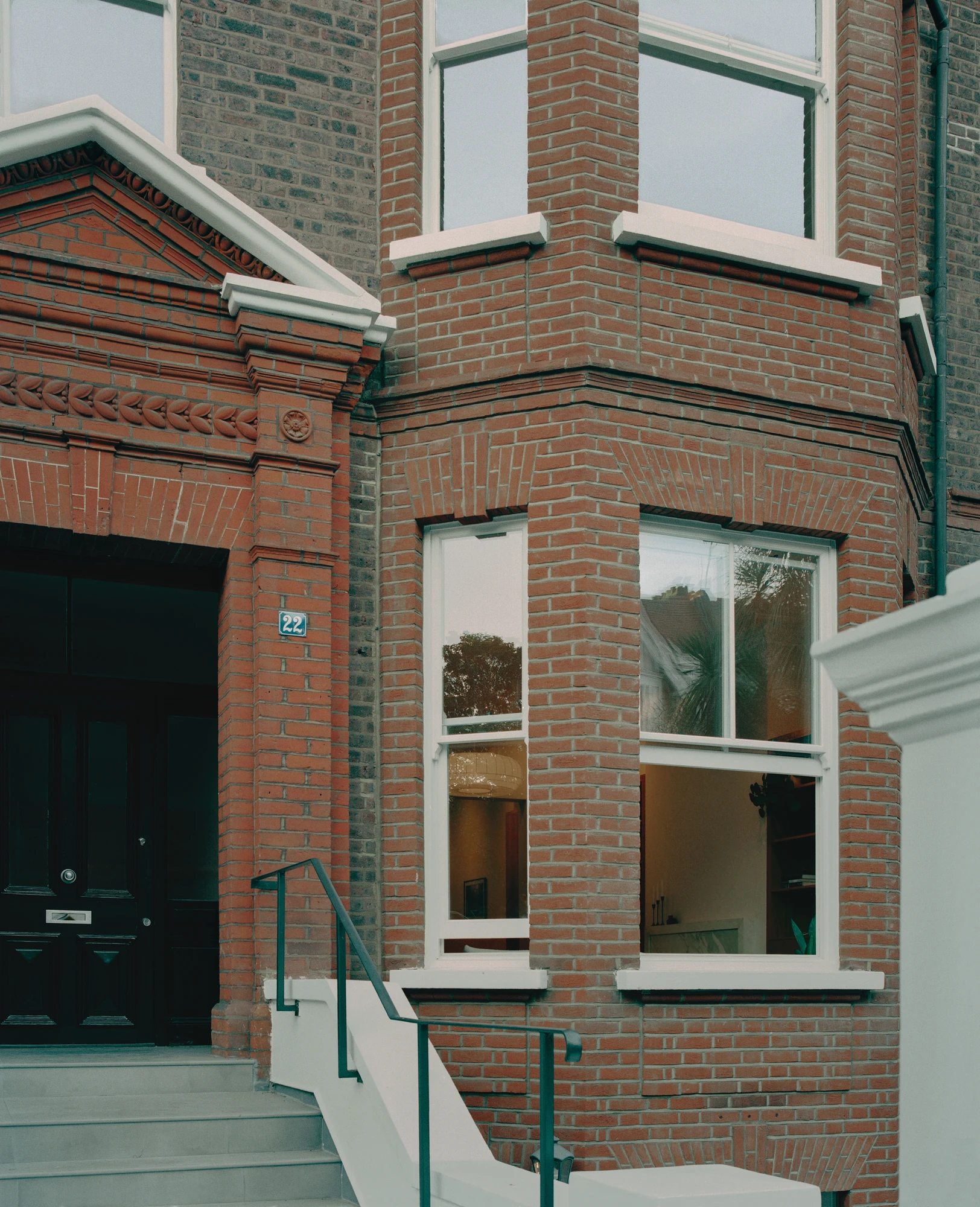 Hampstead House by Twelve Forty One, photographed by Willem Pab — The entrance at close range, a dark panelled front door beside the bay and a stepped approach with a slim handrail.