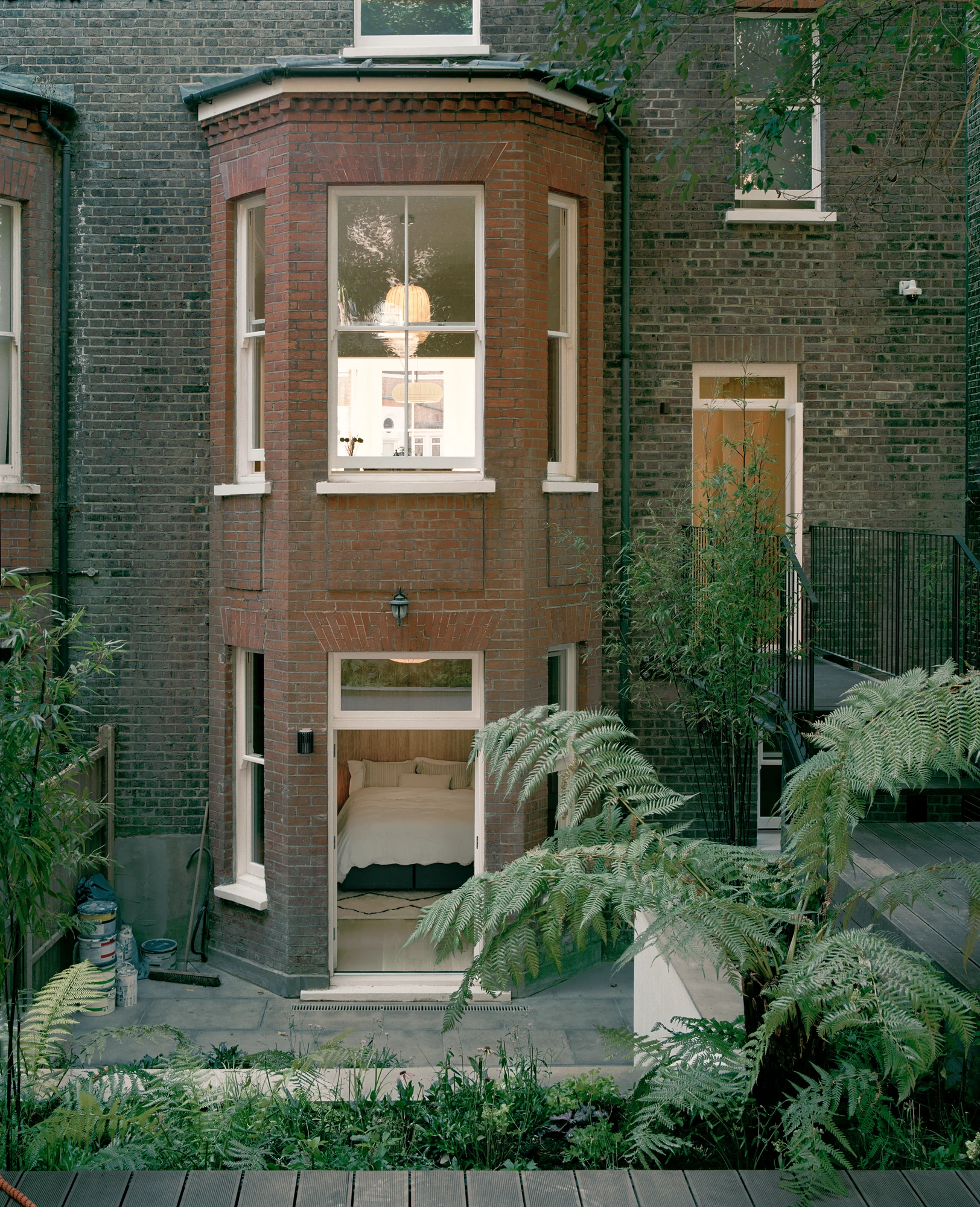 Hampstead House by Twelve Forty One, photographed by Willem Pab — The rear facade straight on, the garden-level bedroom open through its glazed door between beds of planting.