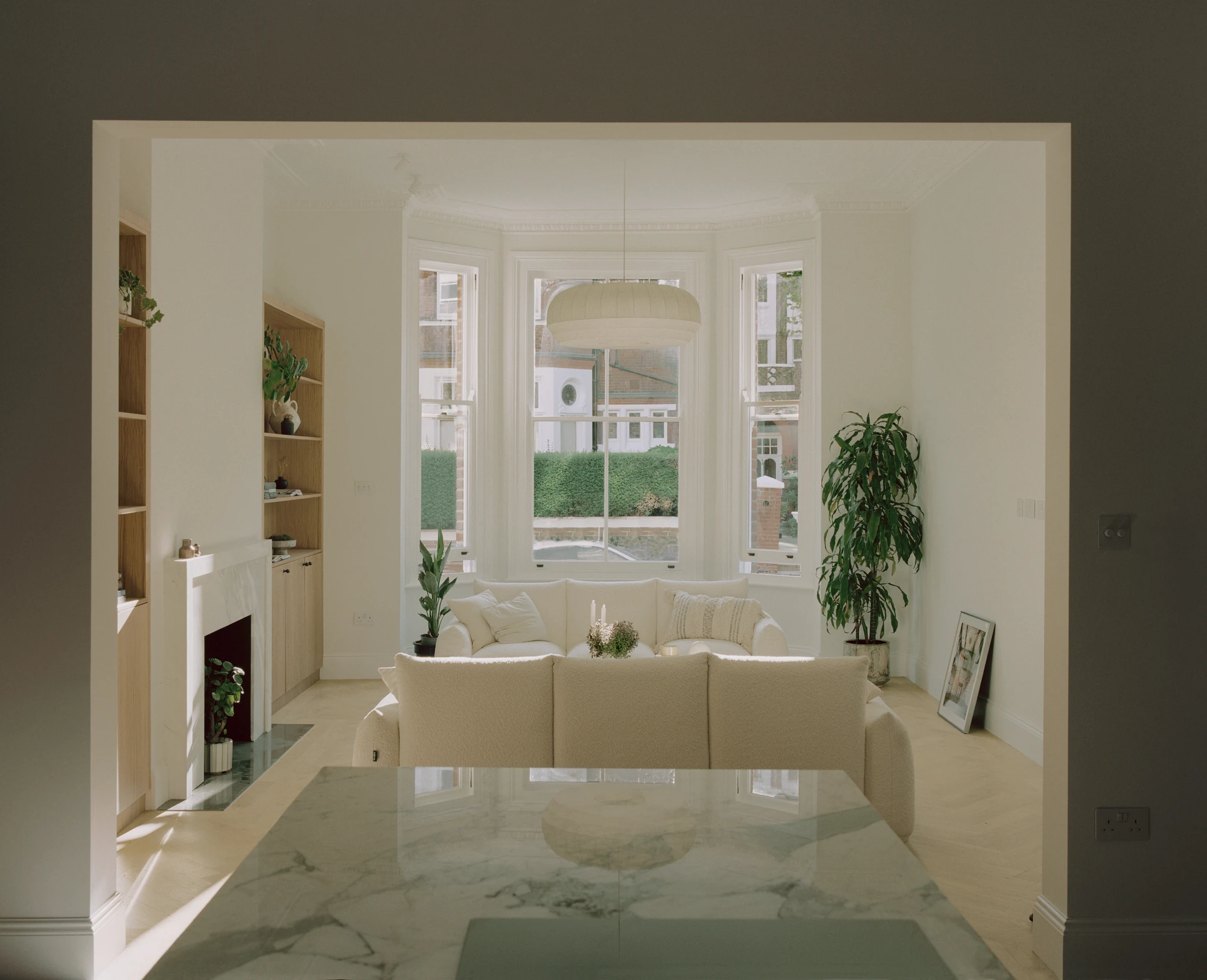 Hampstead House by Twelve Forty One, photographed by Willem Pab — The living room seen through a wide opening, a fireplace flanked by oak shelving and sofas gathered under the bay window.