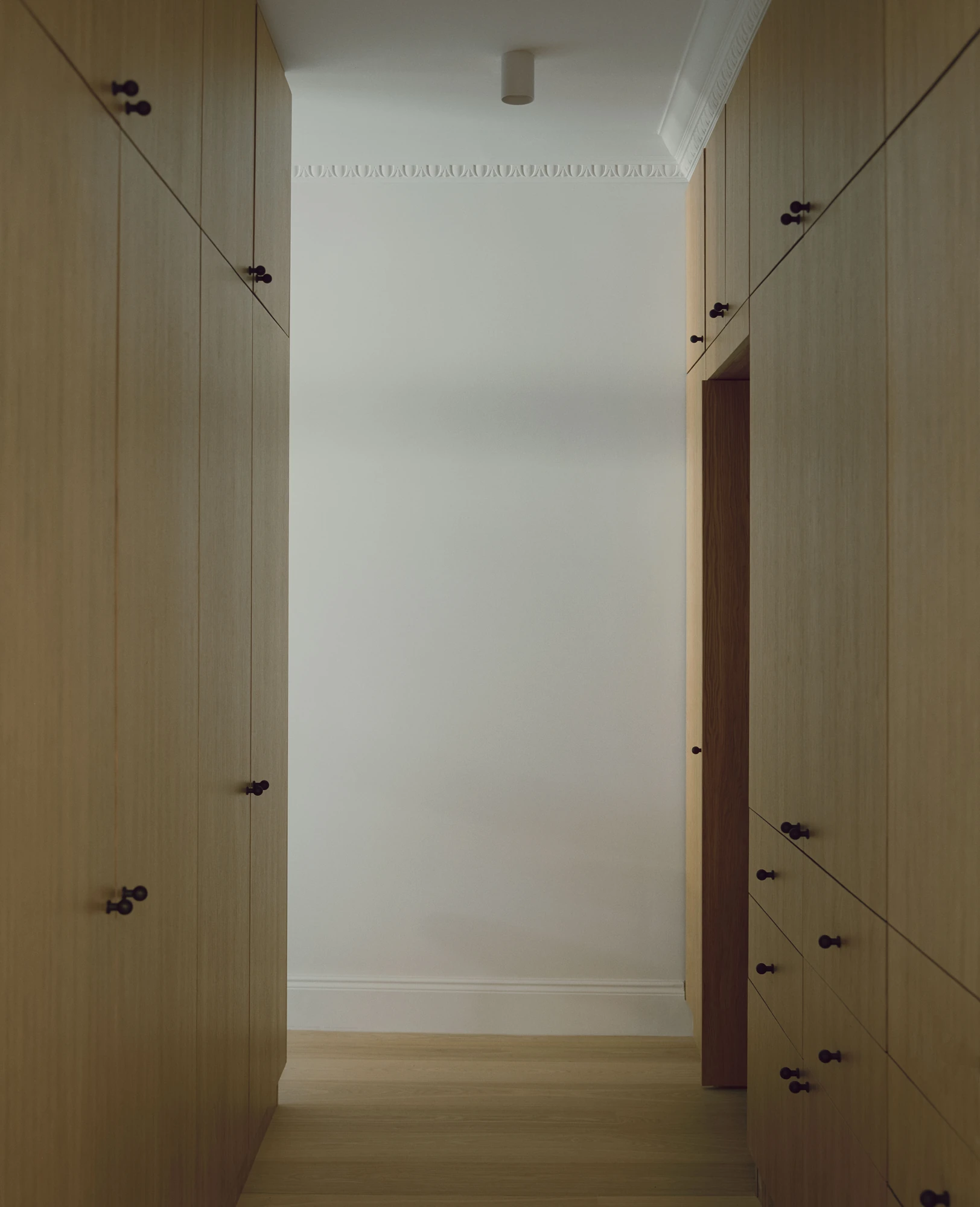 Hampstead House by Twelve Forty One, photographed by Willem Pab — A dressing corridor lined floor to ceiling in oak cabinetry with dark knobs, a cornice running above.