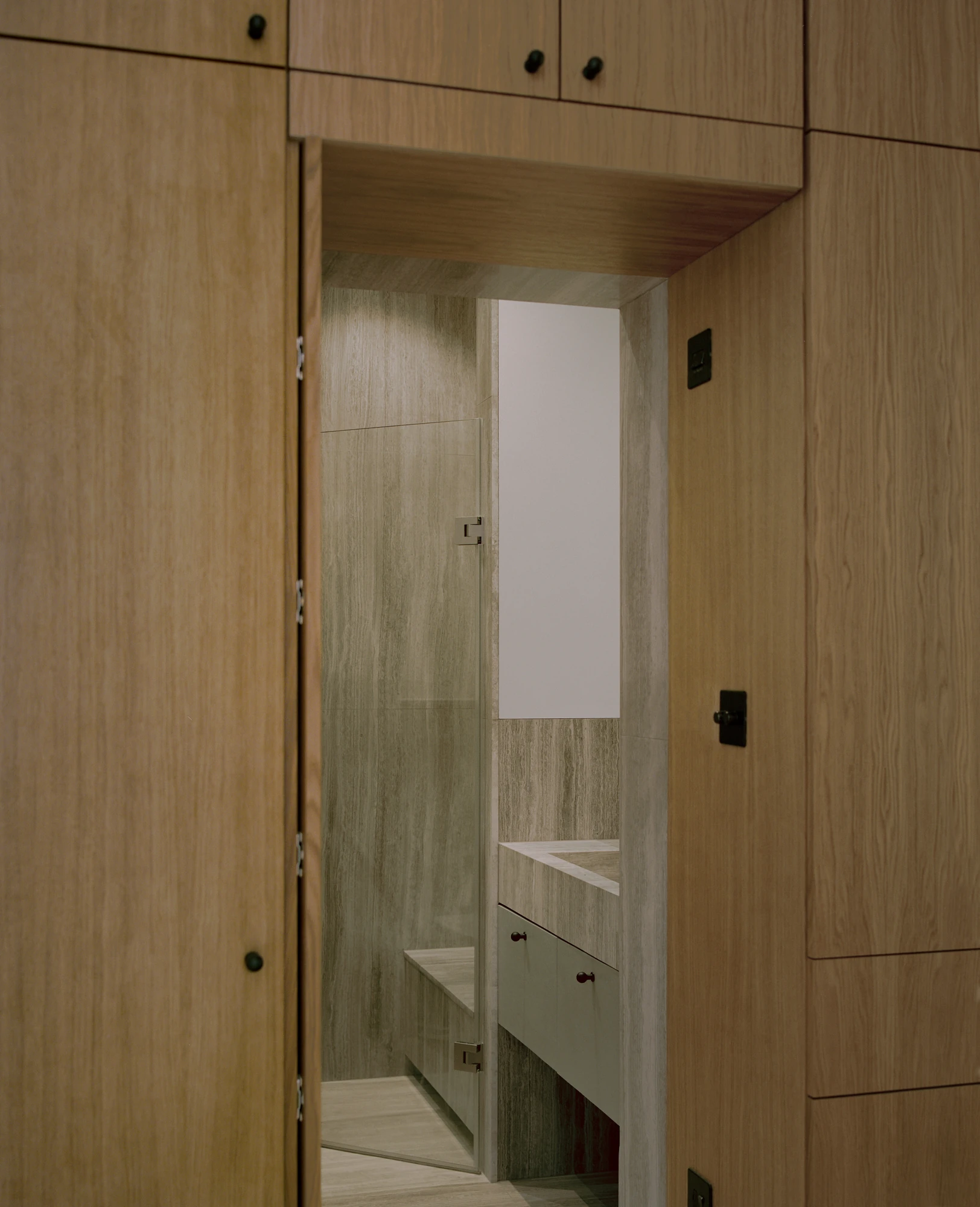 Hampstead House by Twelve Forty One, photographed by Willem Pab — An oak wall of cupboards with a concealed door swung open to a bathroom and its mirrored vanity.