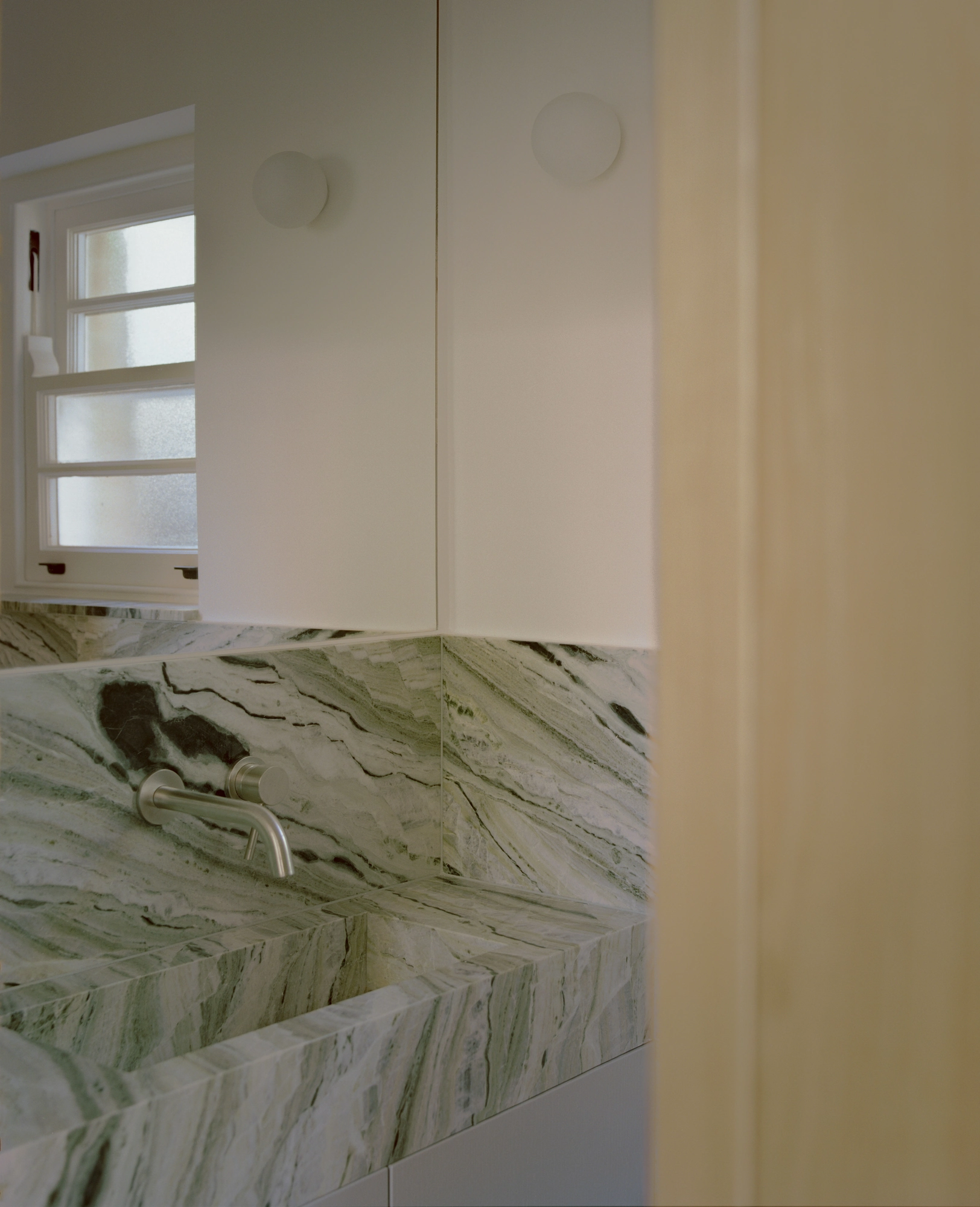 Hampstead House by Twelve Forty One, photographed by Willem Pab — A bathroom basin below an obscured window, a wall-mounted tap above it.