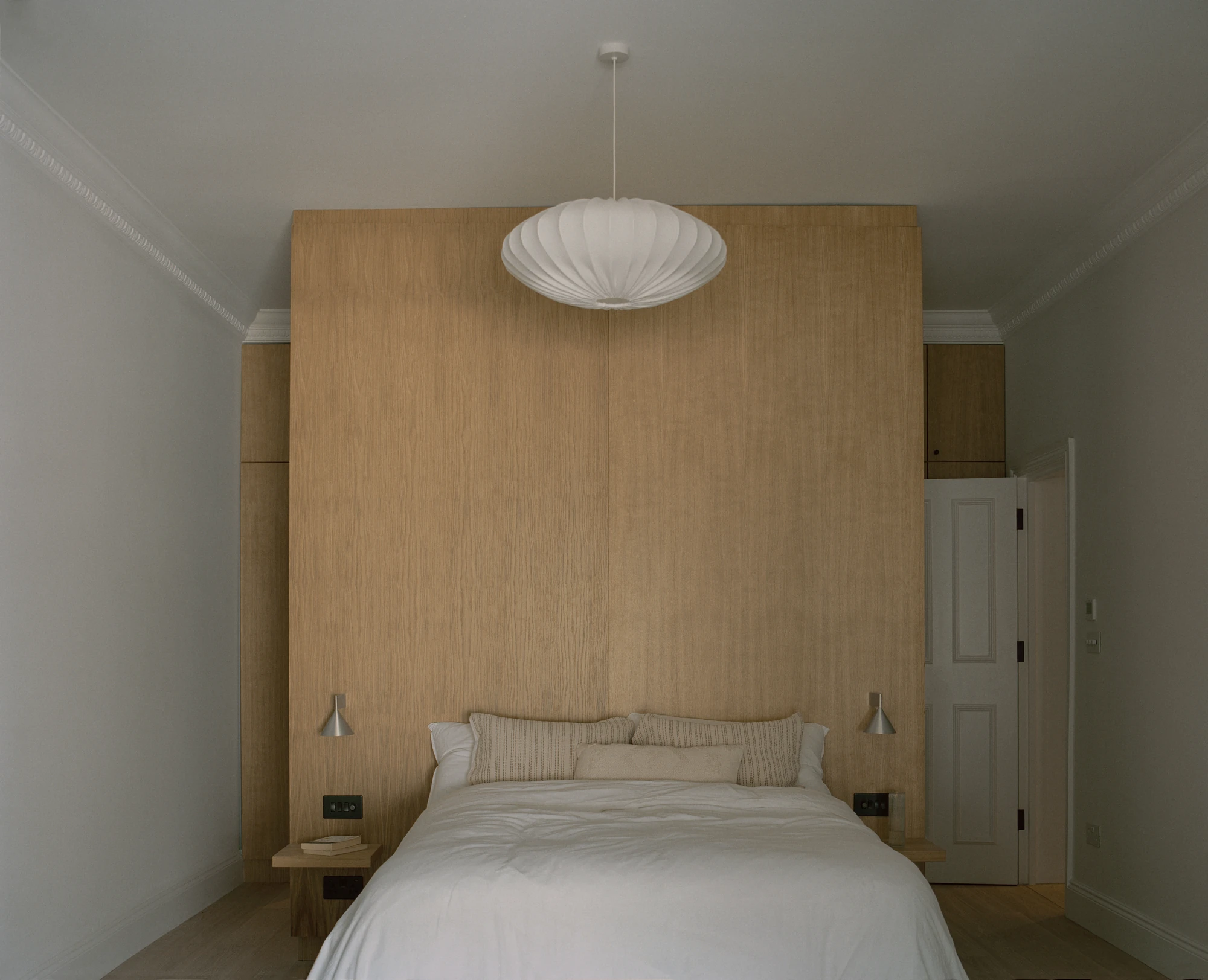 Hampstead House by Twelve Forty One, photographed by Willem Pab — A bedroom with a full-height oak headboard wall, a globe pendant centred above the bed.