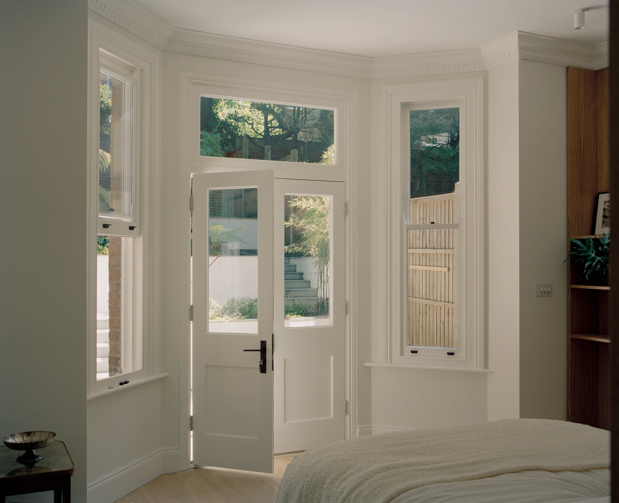 Hampstead House by Twelve Forty One, photographed by Willem Pab — A bedroom opening through glazed double doors onto the garden steps, a cornice tracing the bay.
