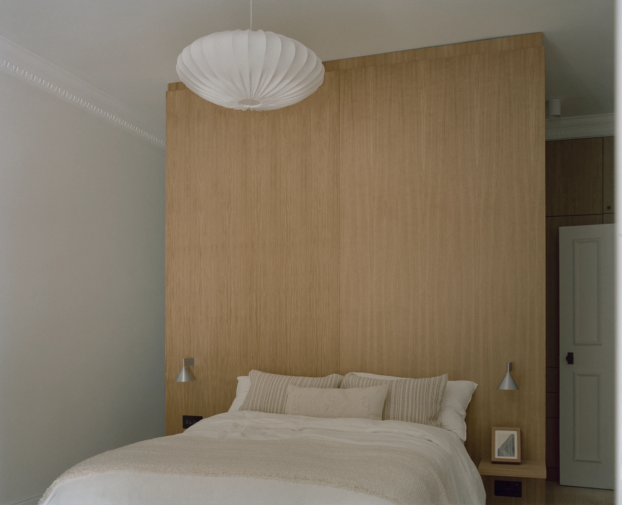 Hampstead House by Twelve Forty One, photographed by Willem Pab — The same bedroom from an angle, the oak headboard wall meeting built-in storage beside a panelled door.