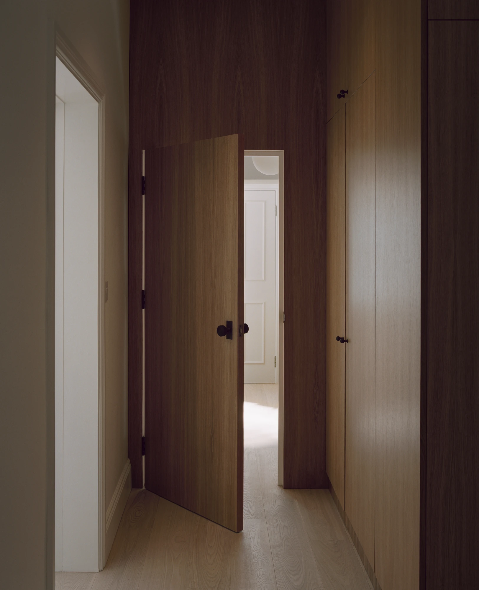Hampstead House by Twelve Forty One, photographed by Willem Pab — A corridor panelled in dark wood, a door ajar onto a brighter landing beyond.