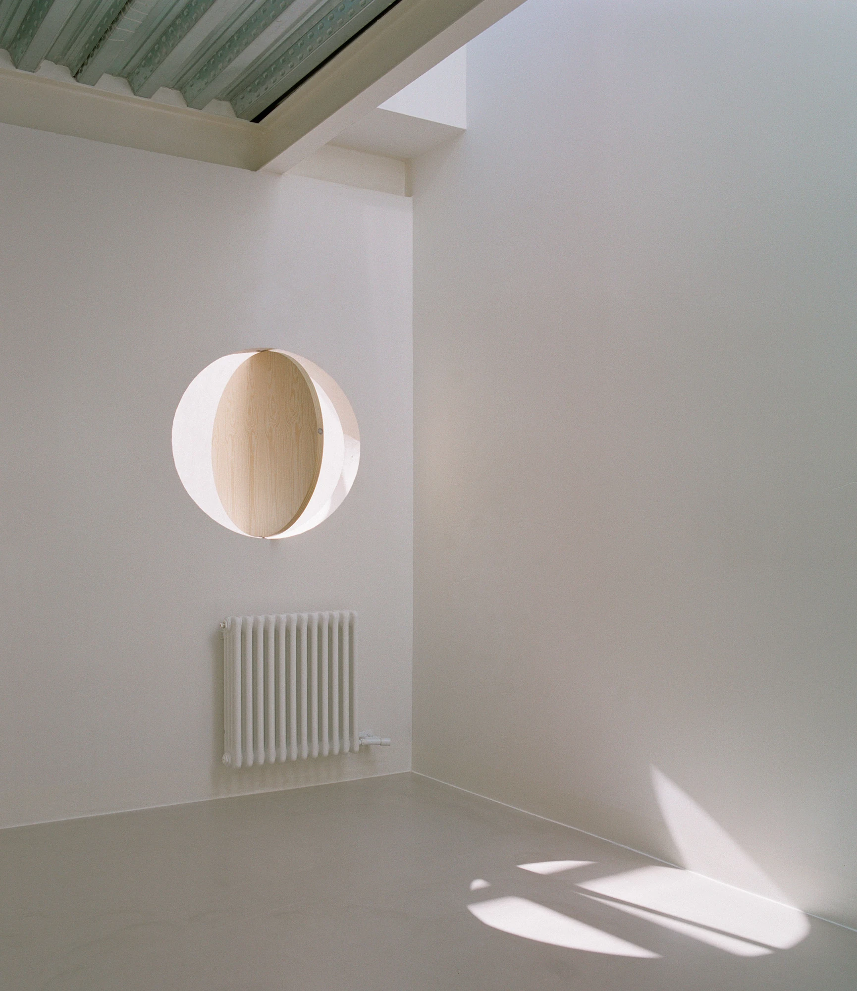 Villa V by Andrea Arriola Fiol and Adrián Mellado Muñoz, photographed by Del Rio Bani — A near-empty upper room with a round opening in one wall and light tracking across the floor