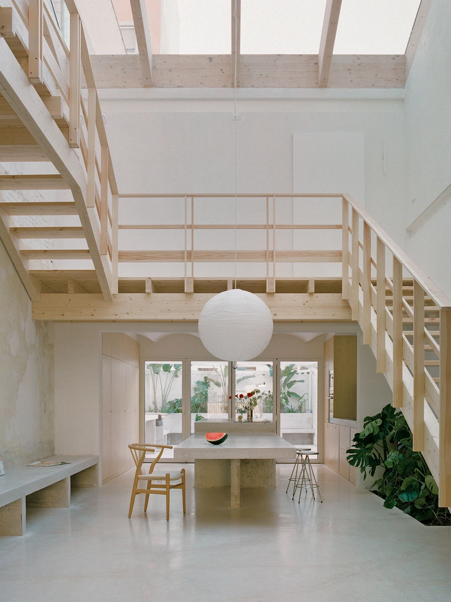 Villa V by Andrea Arriola Fiol and Adrián Mellado Muñoz, photographed by Del Rio Bani — A vertical view through the double-height void, the timber staircase and the concrete table gathered beneath a long skylight