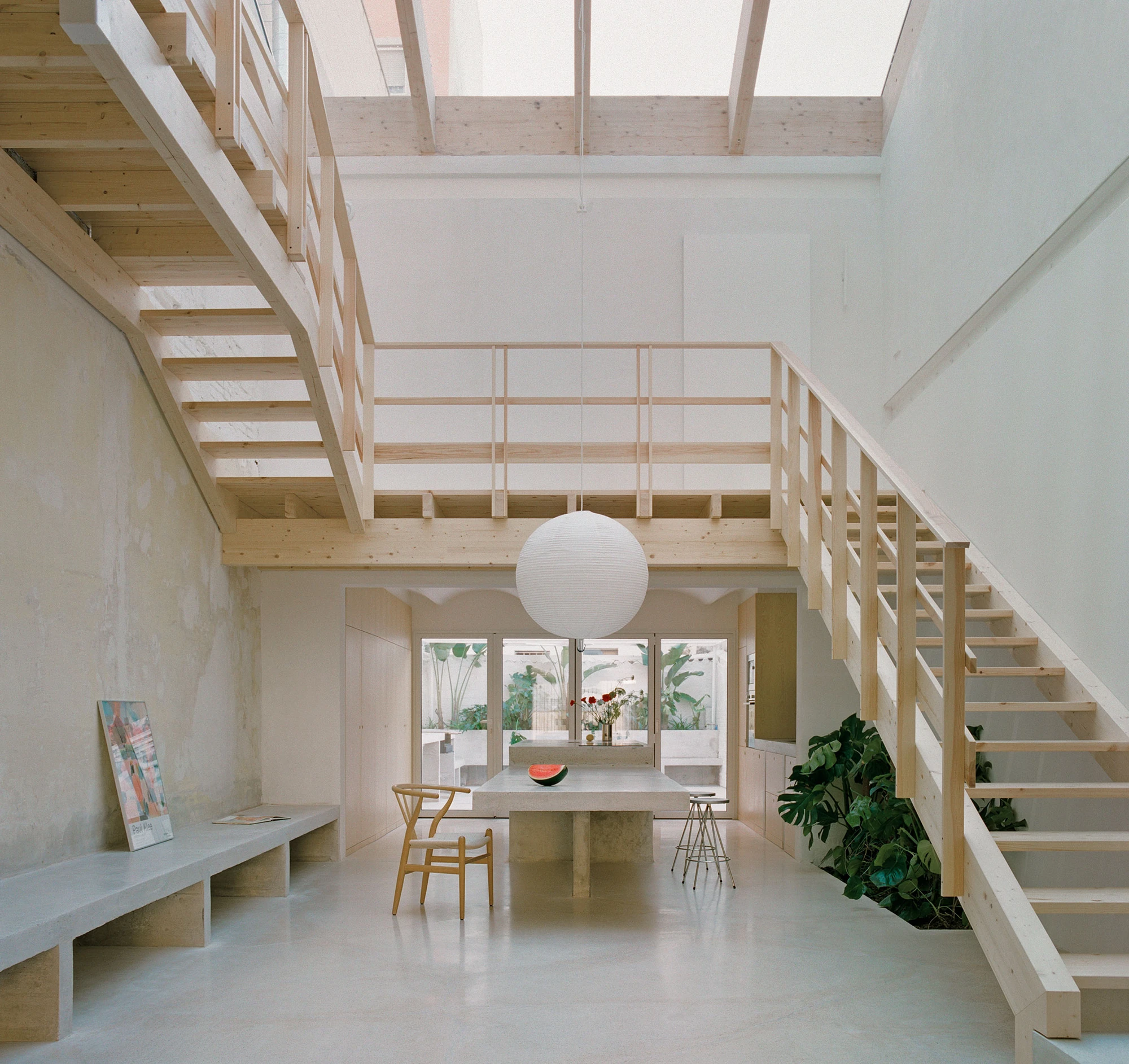 Villa V by Andrea Arriola Fiol and Adrián Mellado Muñoz, photographed by Del Rio Bani — The void seen square-on, twin flights of the timber staircase framing the concrete table at the centre of the plan