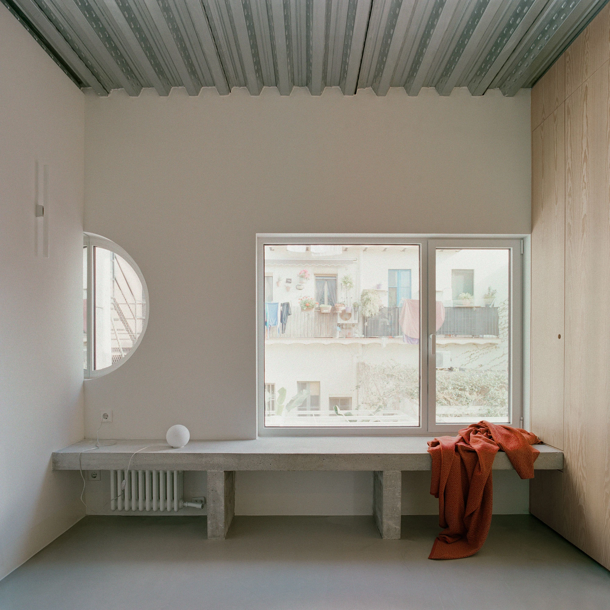 Villa V by Andrea Arriola Fiol and Adrián Mellado Muñoz, photographed by Del Rio Bani — A room on the upper floor with a bench below a wide window and a round window set into the adjoining wall