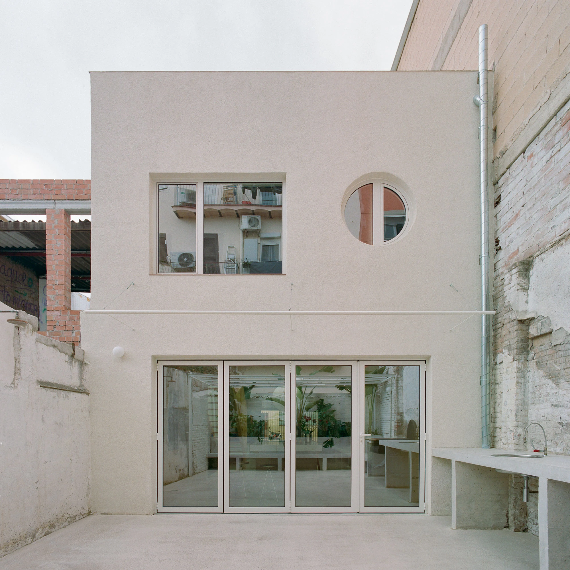 Villa V by Andrea Arriola Fiol and Adrián Mellado Muñoz, photographed by Del Rio Bani — The rear facade on the patio, glazed doors opening the ground floor and a round window above
